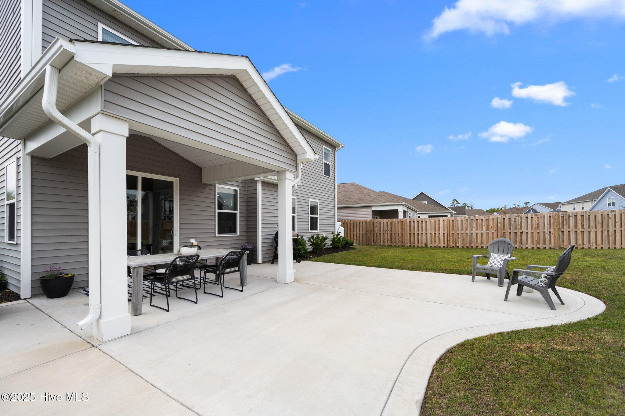 Covered patio with outdoor dining set beside a curved concrete seating area and fenced backyard.