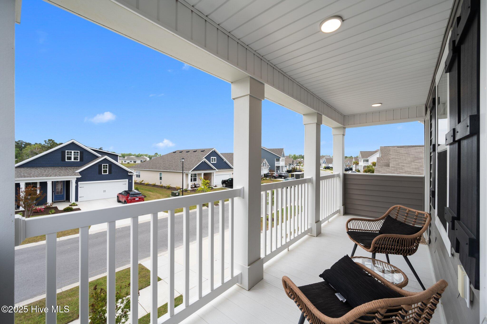 Covered porch with wicker seating and white railings overlooking a residential neighborhood.