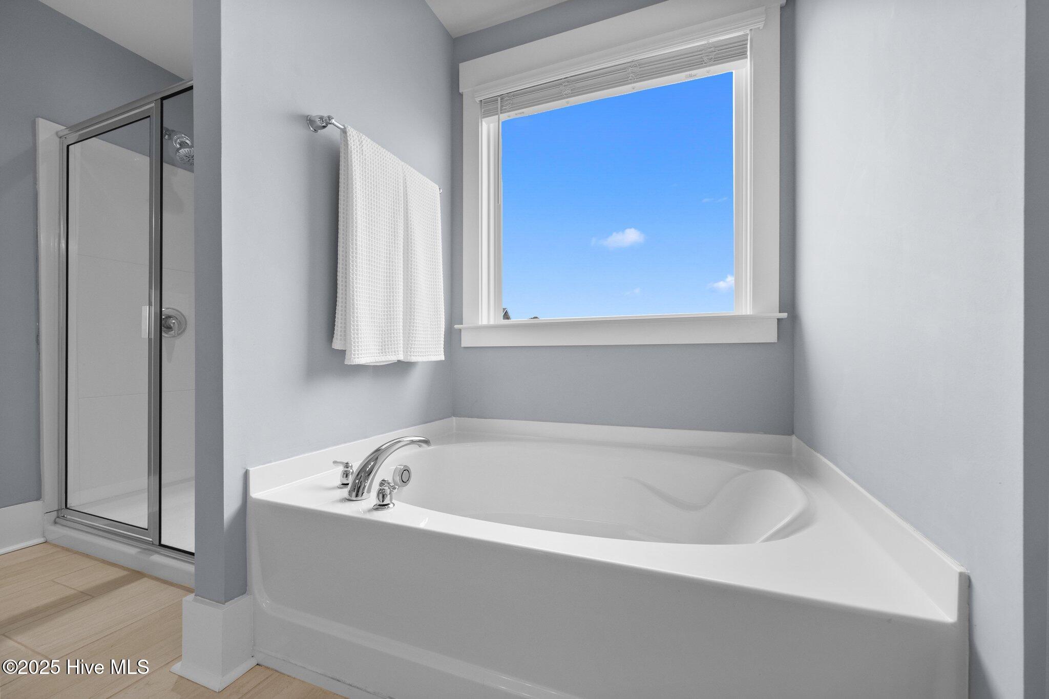 Bathroom with a large soaking tub beneath a window beside a glass-enclosed shower.