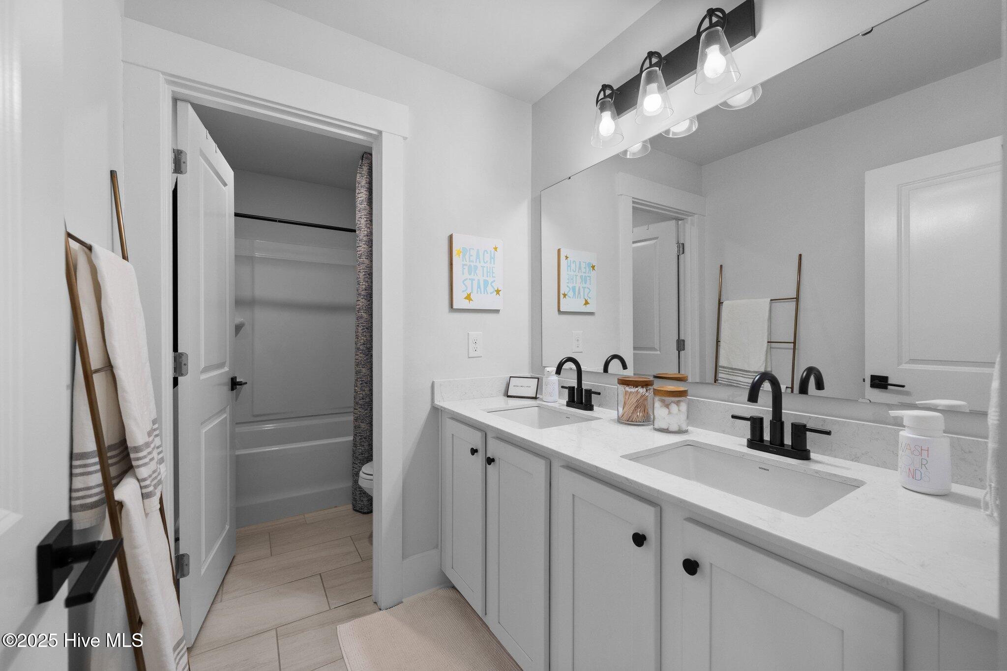 Bathroom with a double-sink white vanity, black faucets, and an open doorway to the tub and shower.