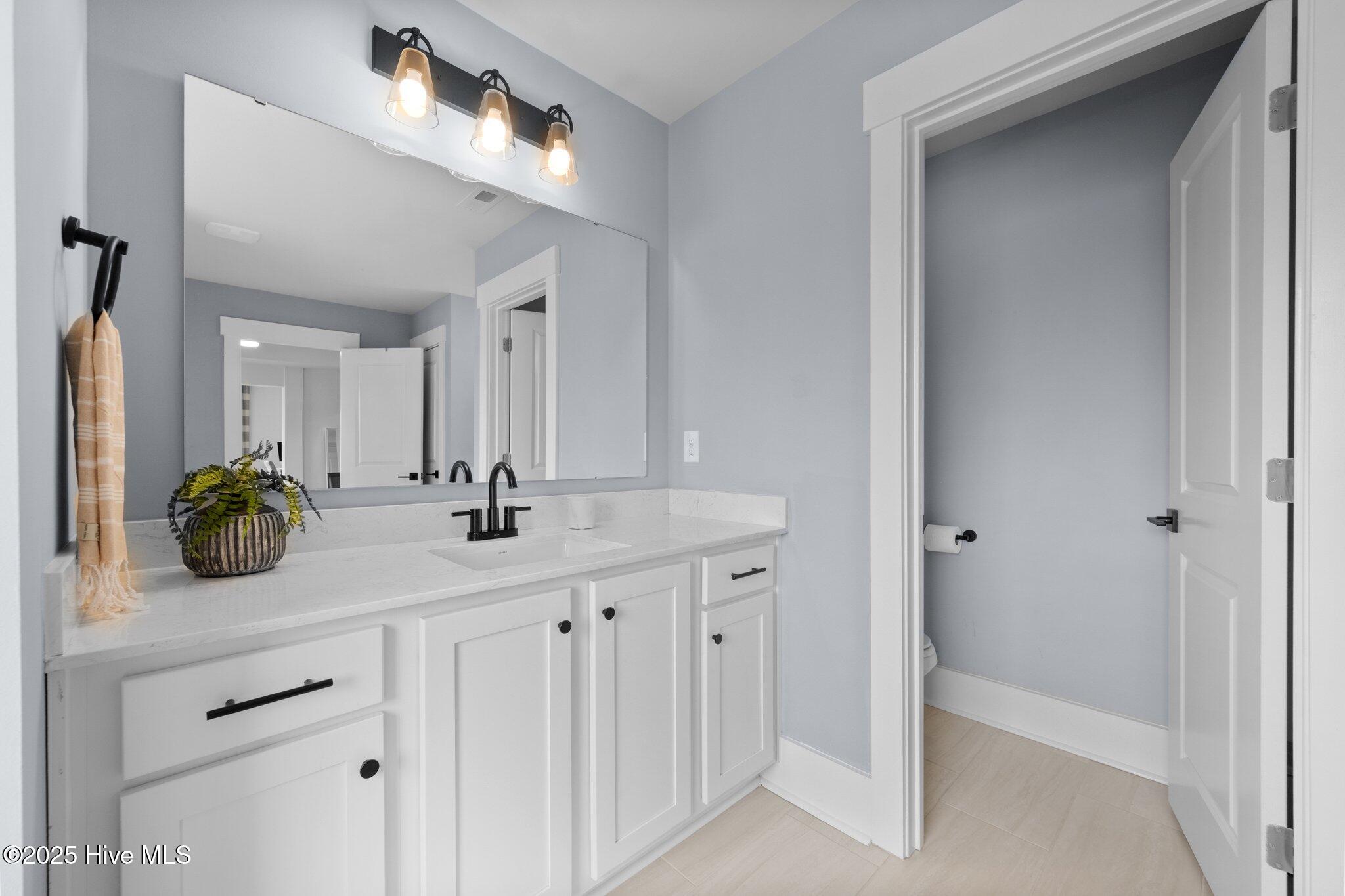 Bathroom vanity with a large mirror, black fixtures, and an open doorway to a separate toilet area.
