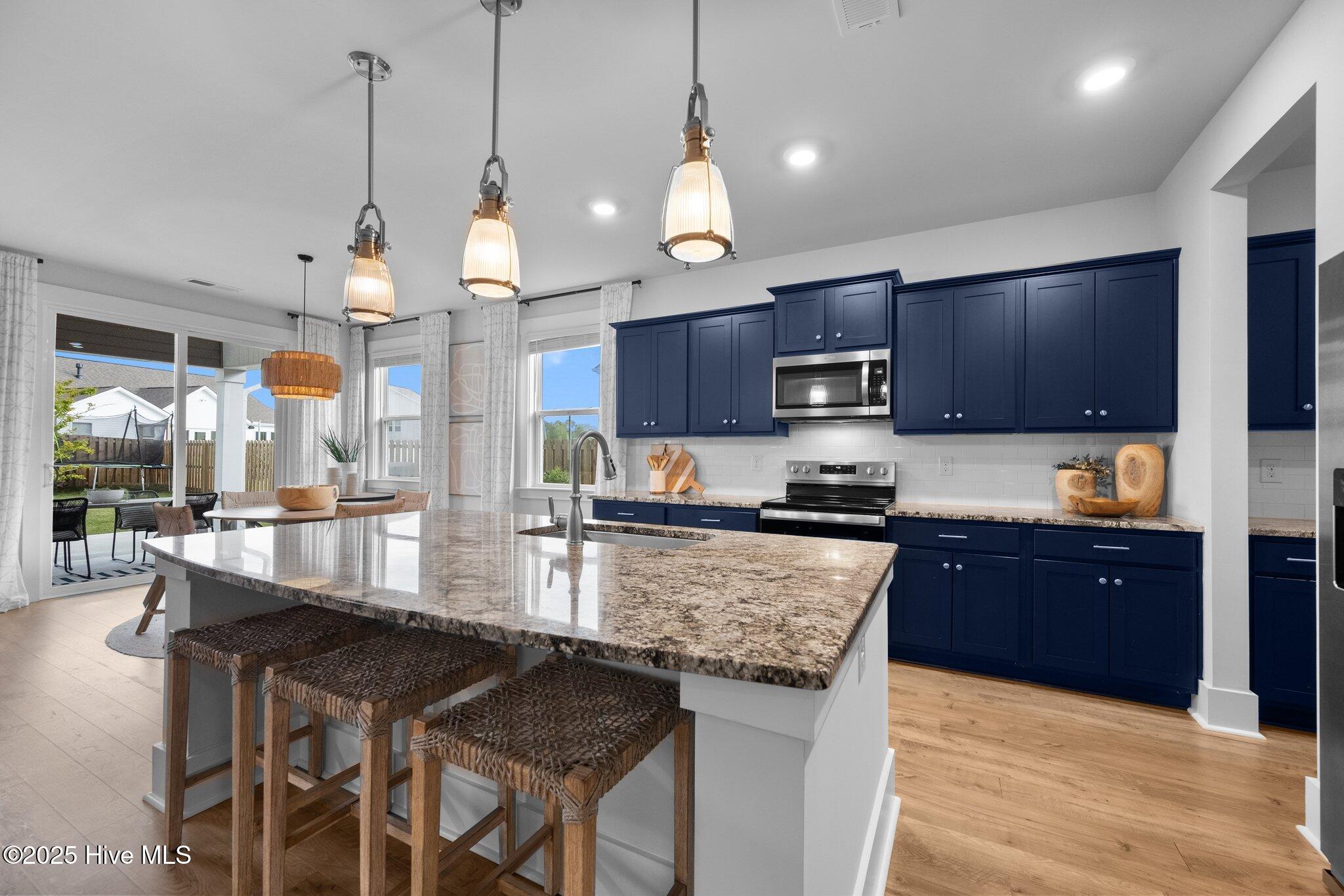 Kitchen with navy cabinets, a granite island, woven bar stools, and sliding doors to the backyard.
