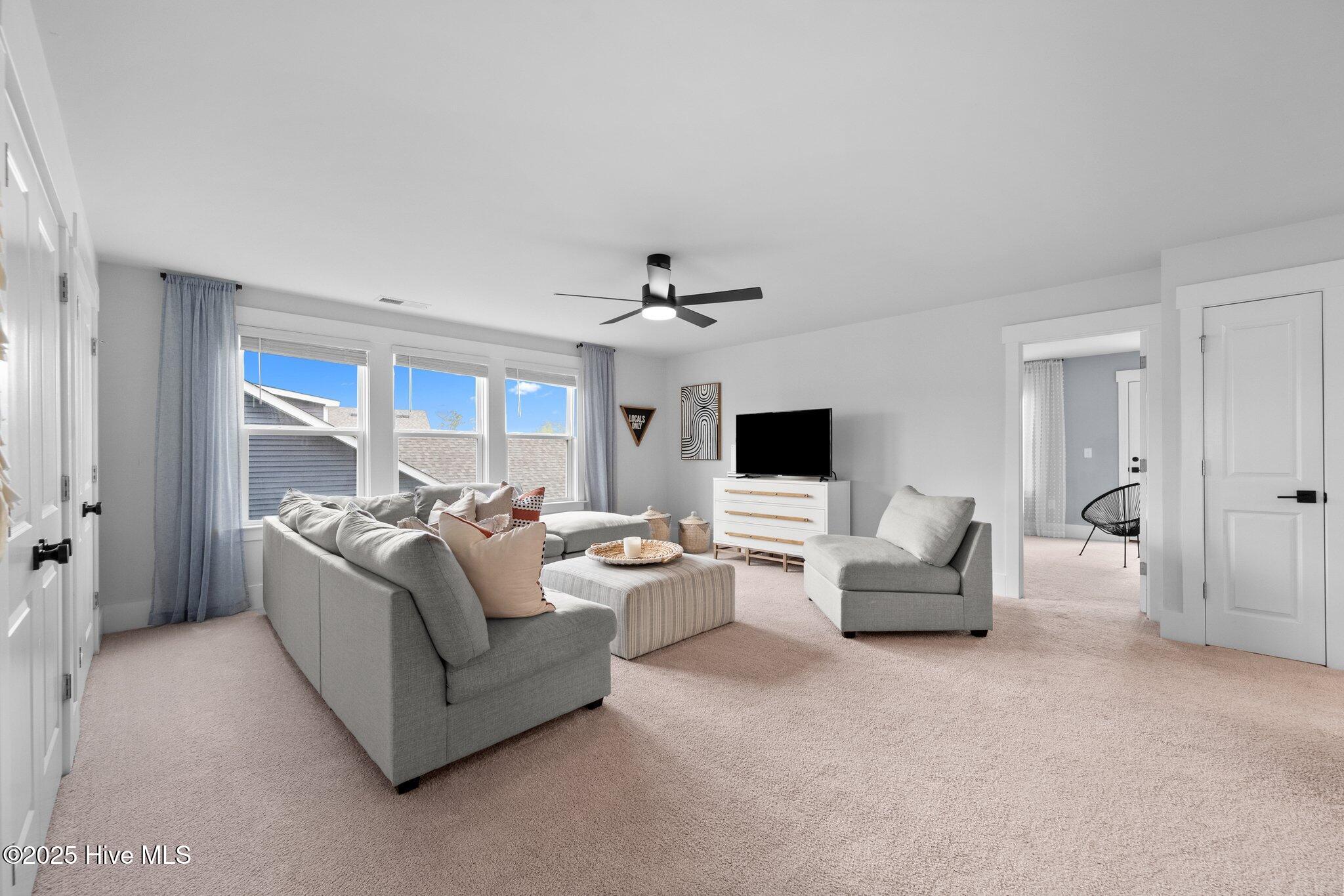 Furnished living room with a gray sectional, striped ottoman, and large sunny windows.