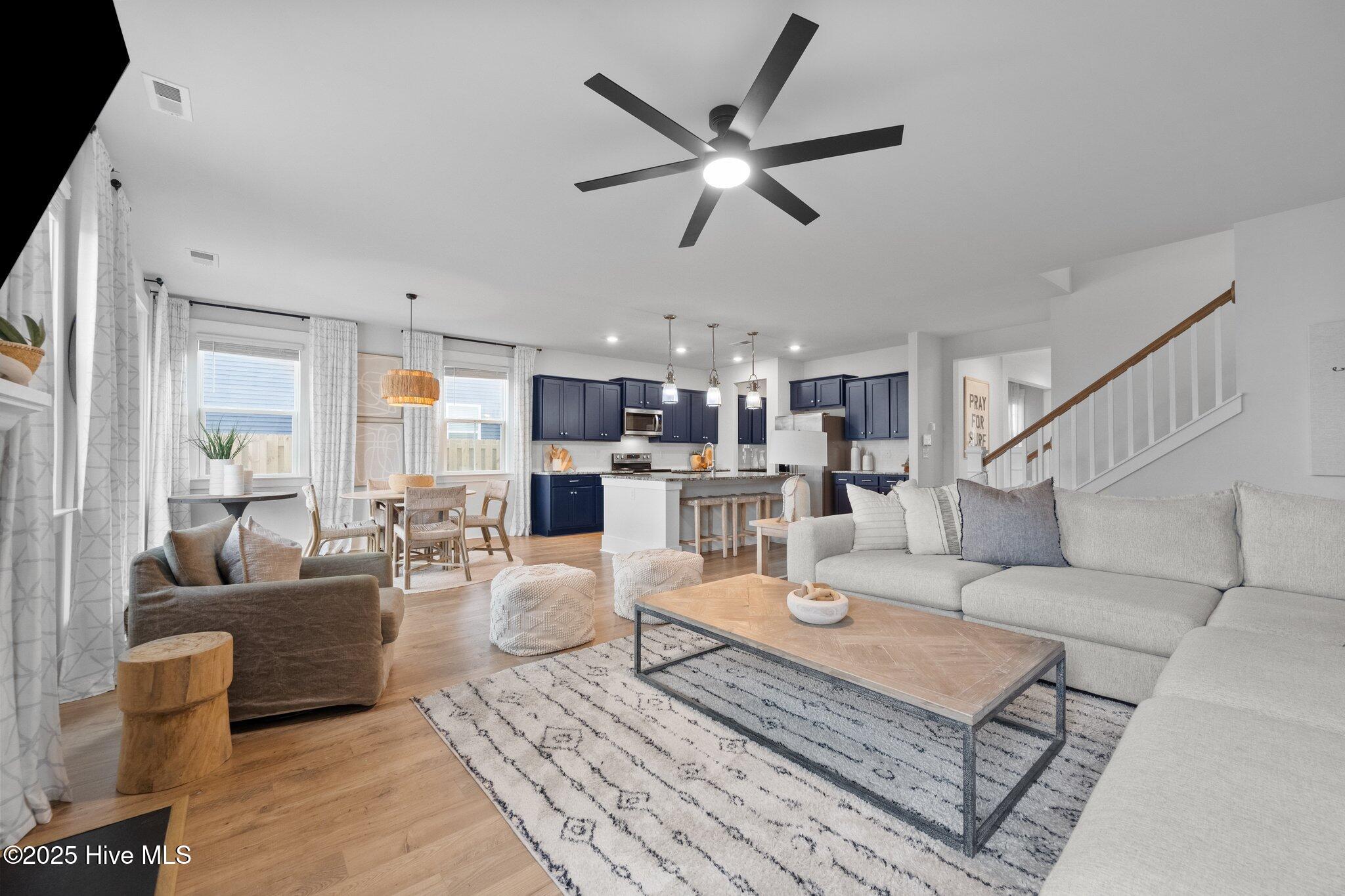 Open-plan living room and kitchen with navy cabinets, a large sectional, and a staircase.