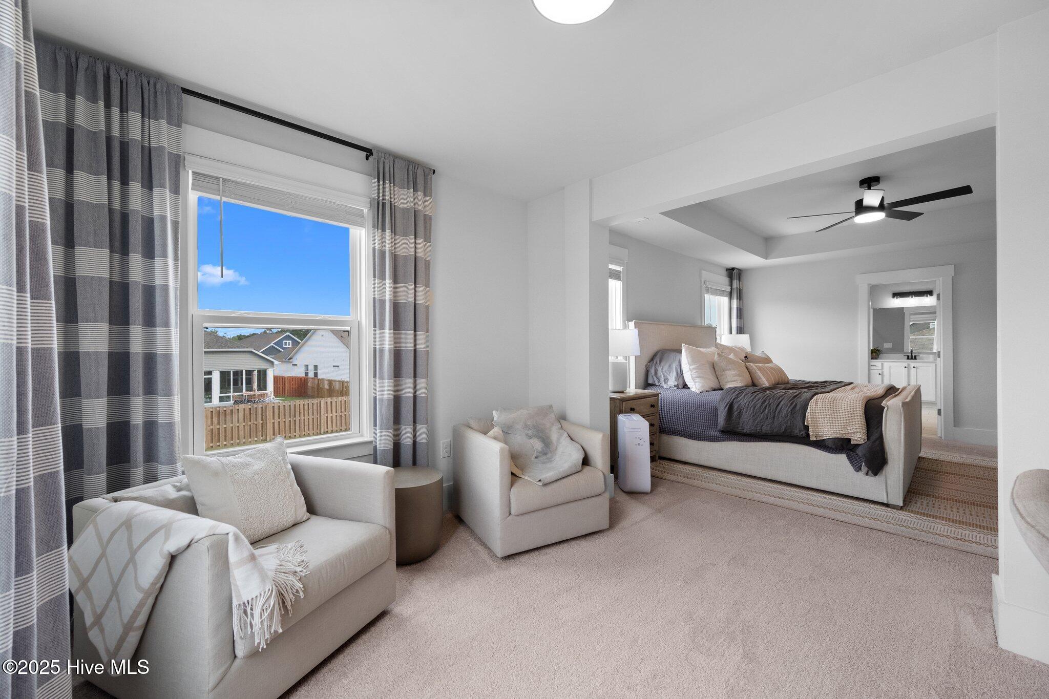 Staged bedroom with a large bed, adjoining sitting area, and doorway to an ensuite bathroom.