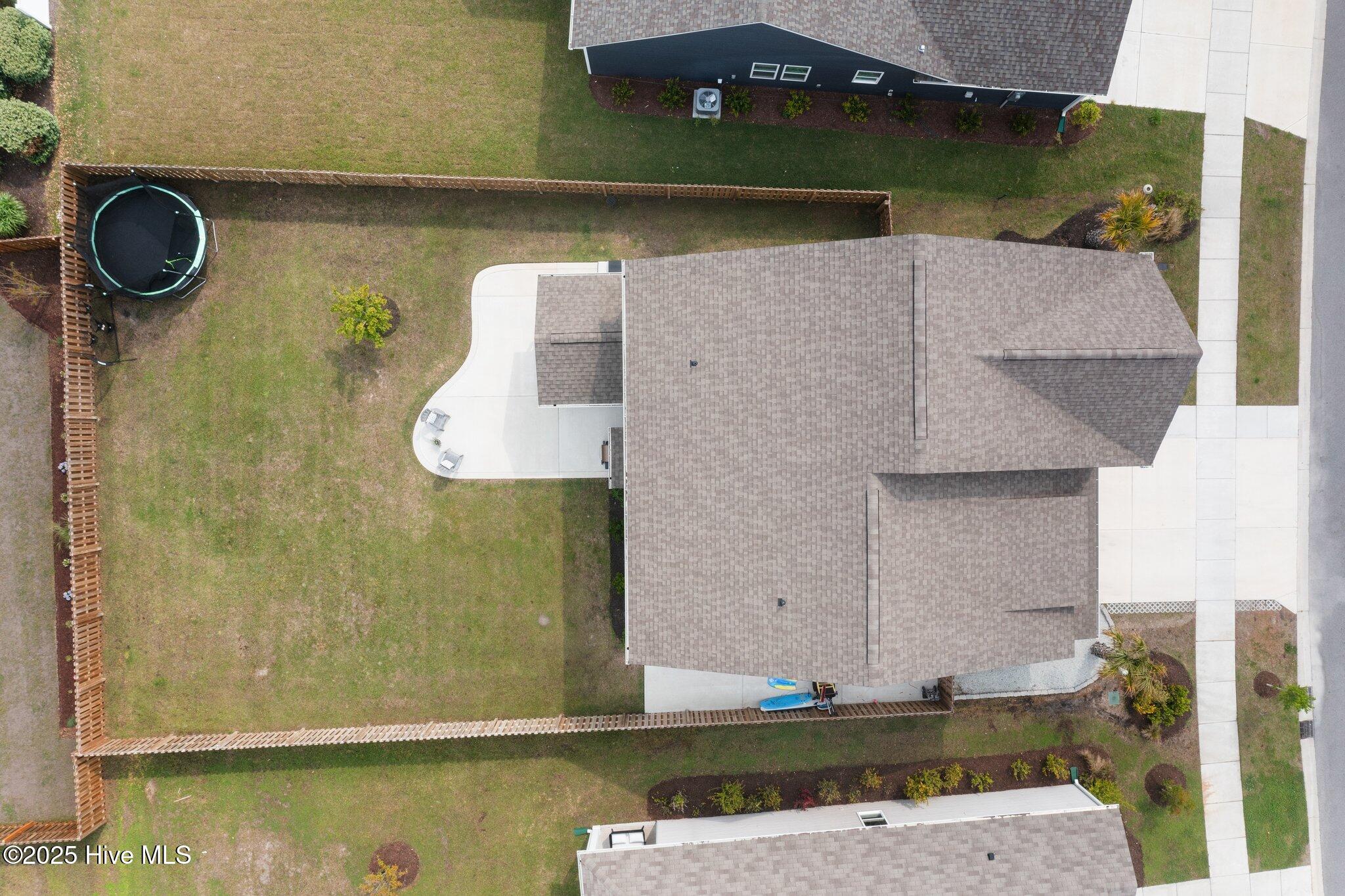 Aerial view of a home with a fenced lawn, trampoline, and curved concrete patio.