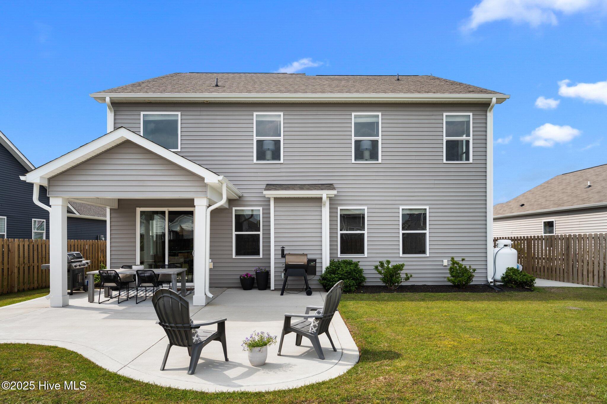 Two-story gray home with a covered patio, outdoor dining set, lounge chairs, and lawn.