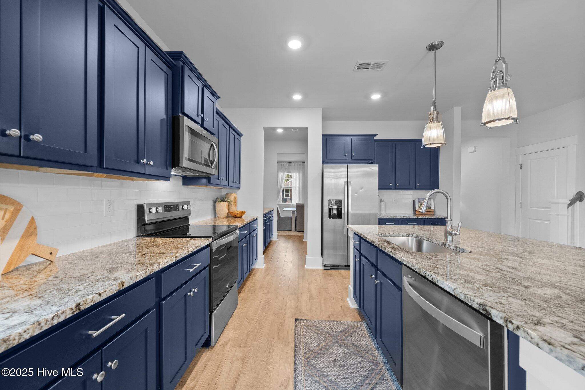 Kitchen with navy cabinets, granite countertops, stainless steel appliances, and a large island with a sink.