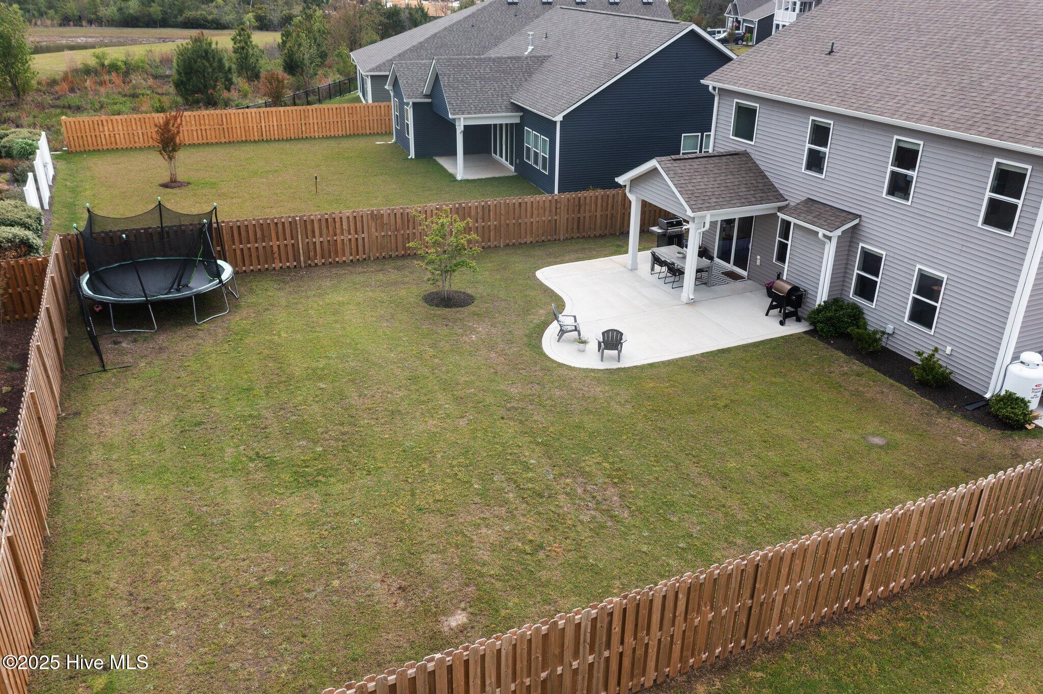 Fenced backyard with a large lawn, trampoline, and curved patio beside the home.