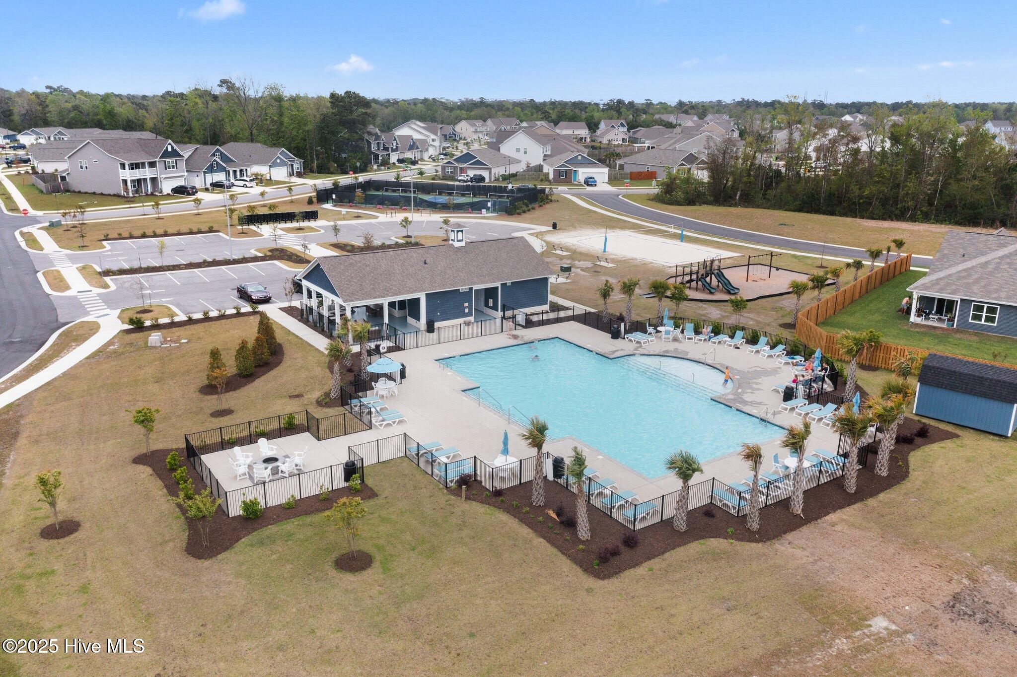 Community pool and clubhouse with a playground and court, viewed from above among neighborhood homes.