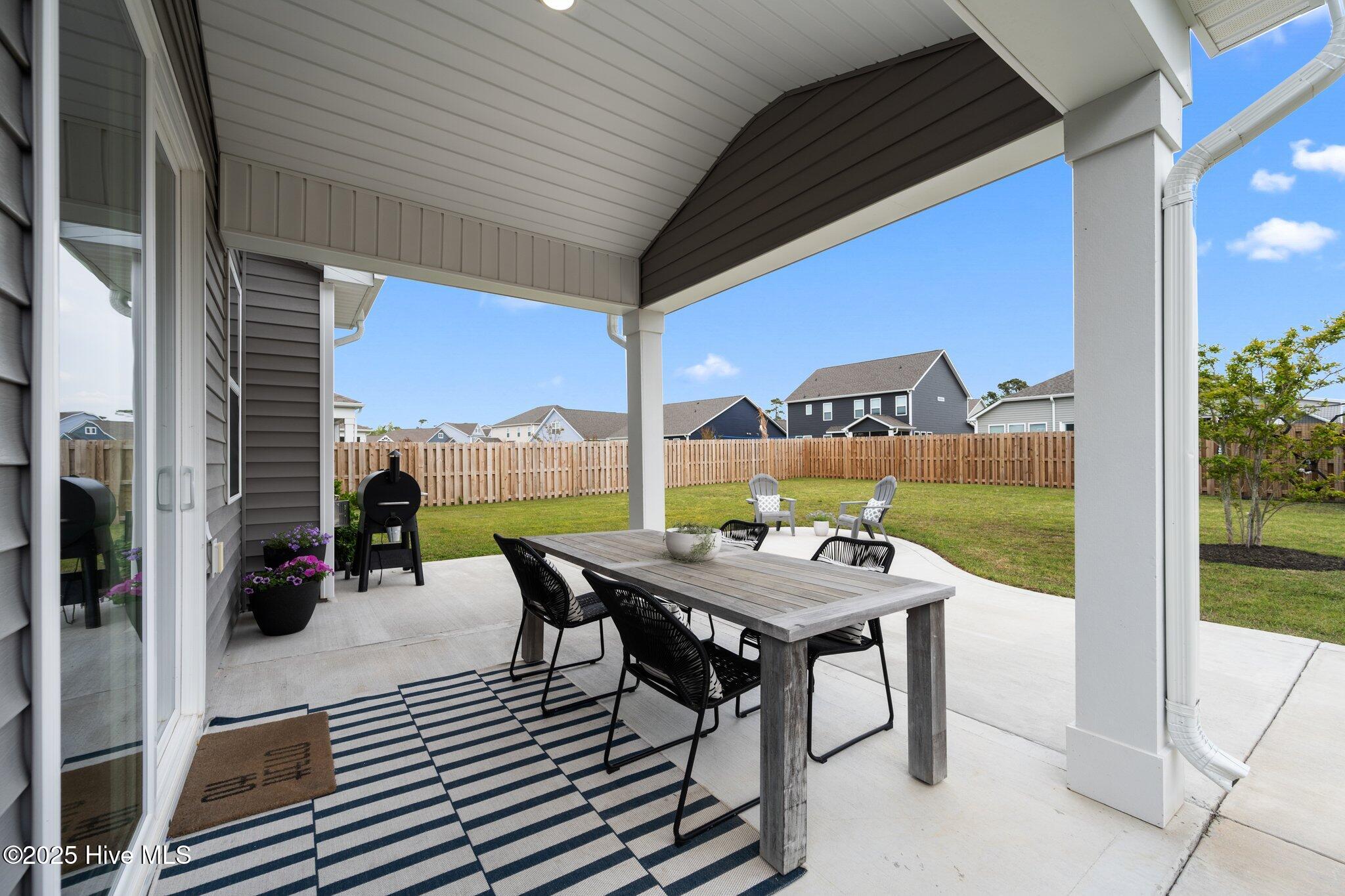 Covered patio with outdoor dining set and grill overlooking a fenced backyard.