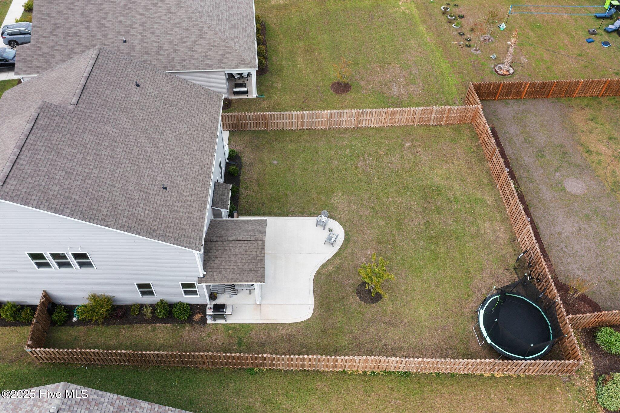 Fenced backyard with a curved patio and round trampoline beside the home.