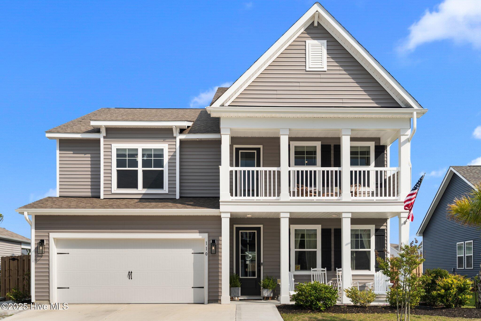 Two-story gray home with white double porches, an attached garage, and an American flag.