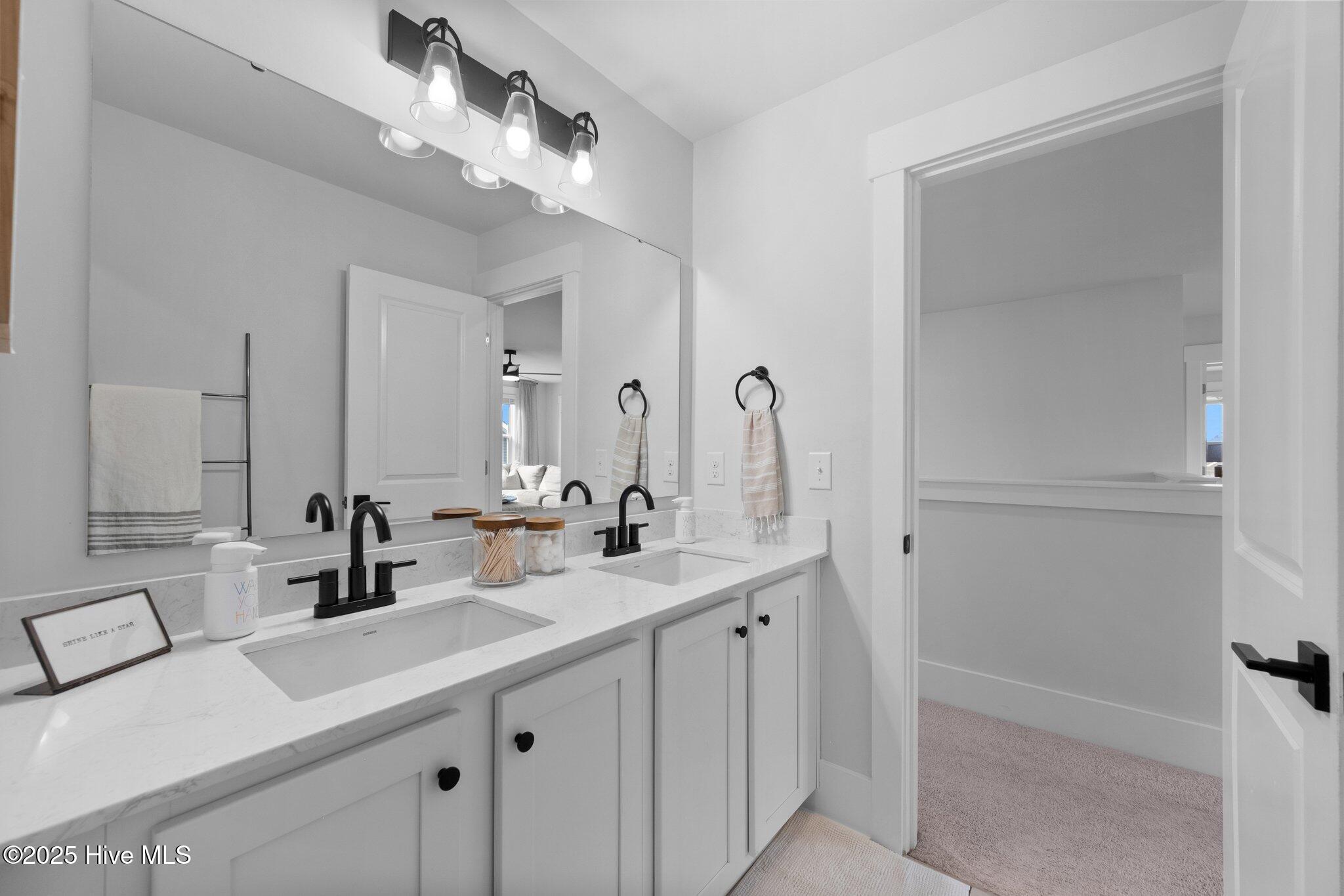 Bathroom with a long double vanity, marble-look counters, black faucets, and a large mirror.