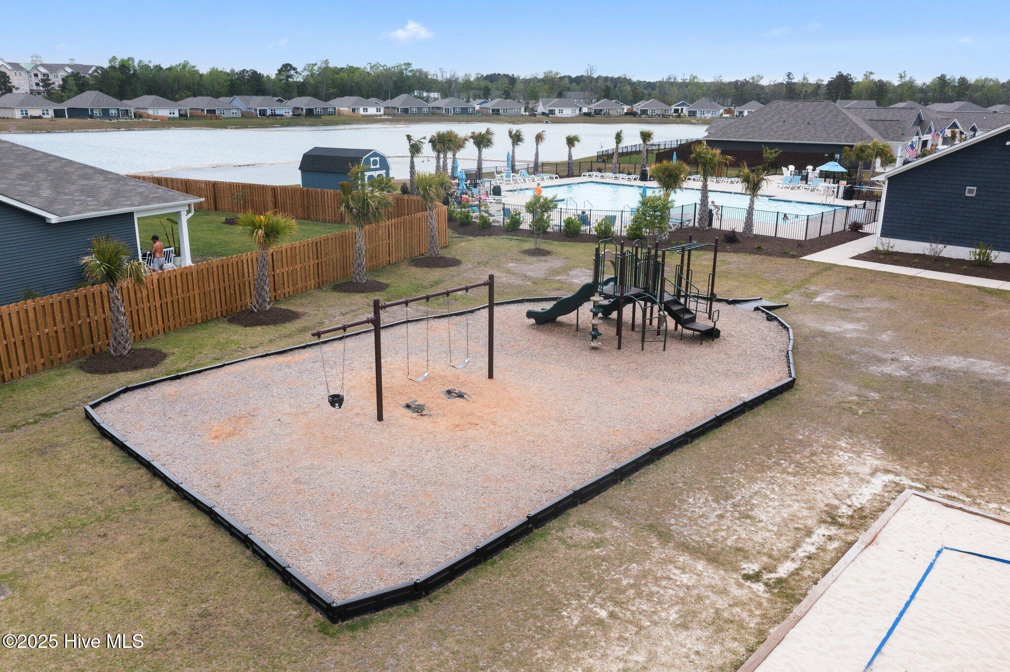 Community playground with swings and climbing equipment beside a pool and lake.