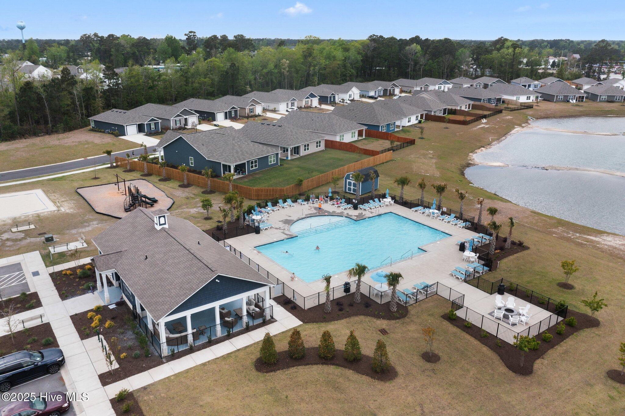 Aerial view of a community pool and pavilion surrounded by homes, with a pond beyond.
