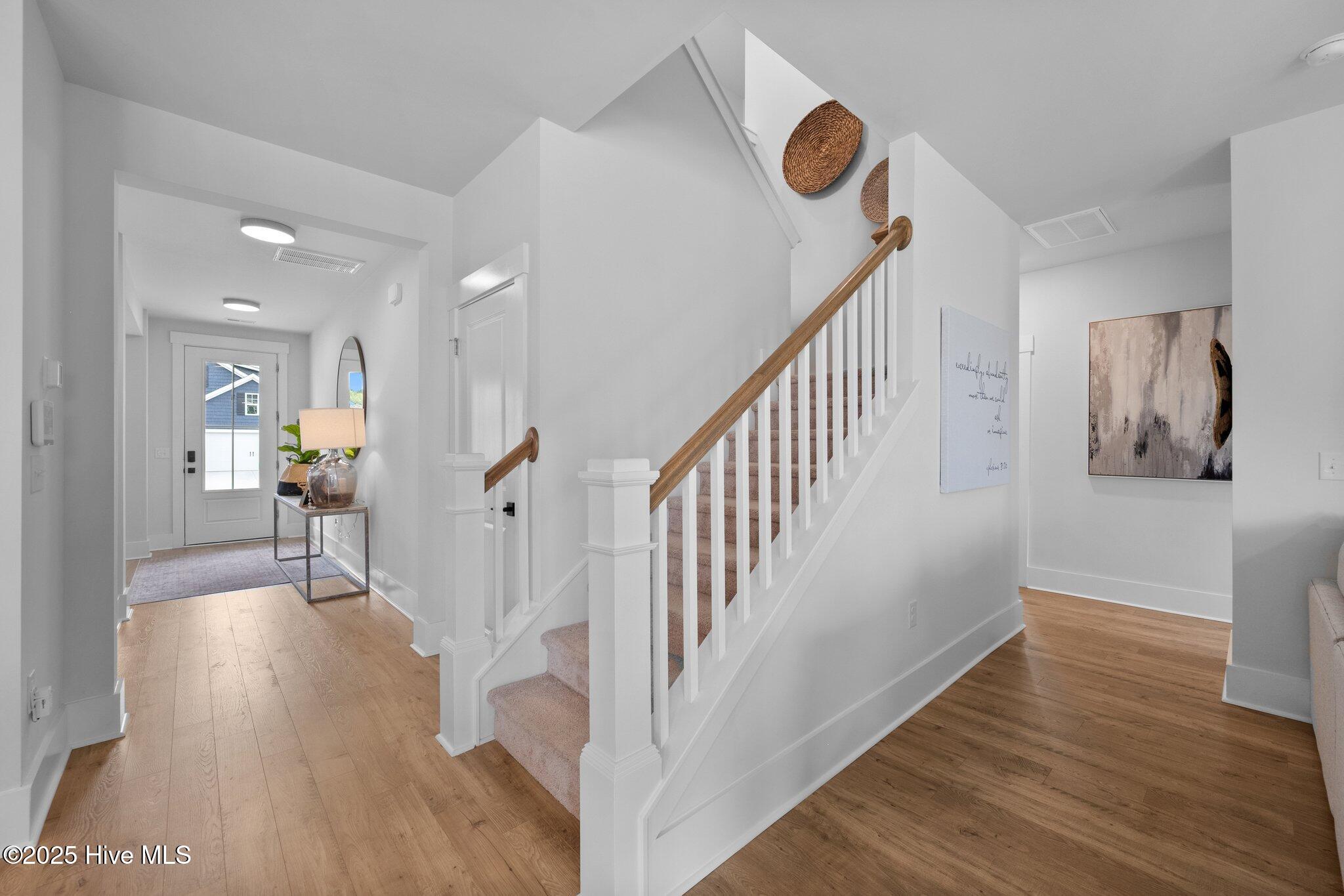 Bright entry foyer with a carpeted staircase, wood handrail, and light wood floors.