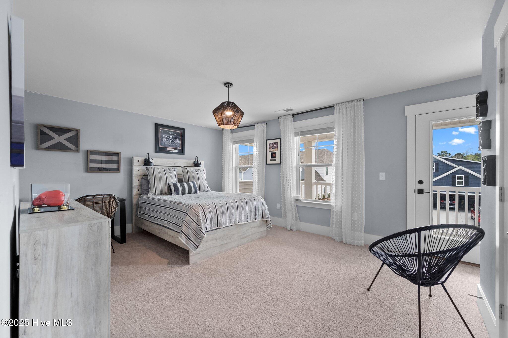 Furnished bedroom with a striped bed, sheer curtains, and a black woven chair beside the glass door.