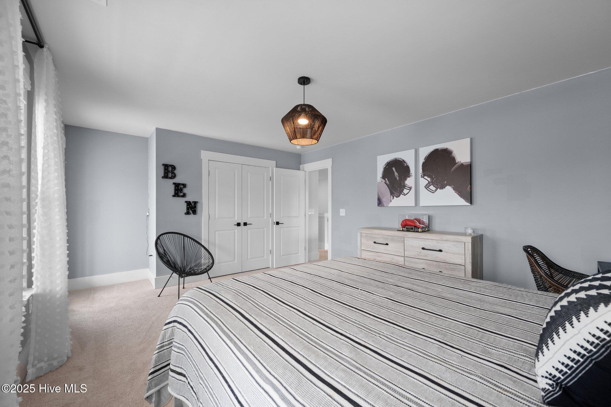 Bedroom with a striped bed, football helmet artwork, and a light wood dresser.