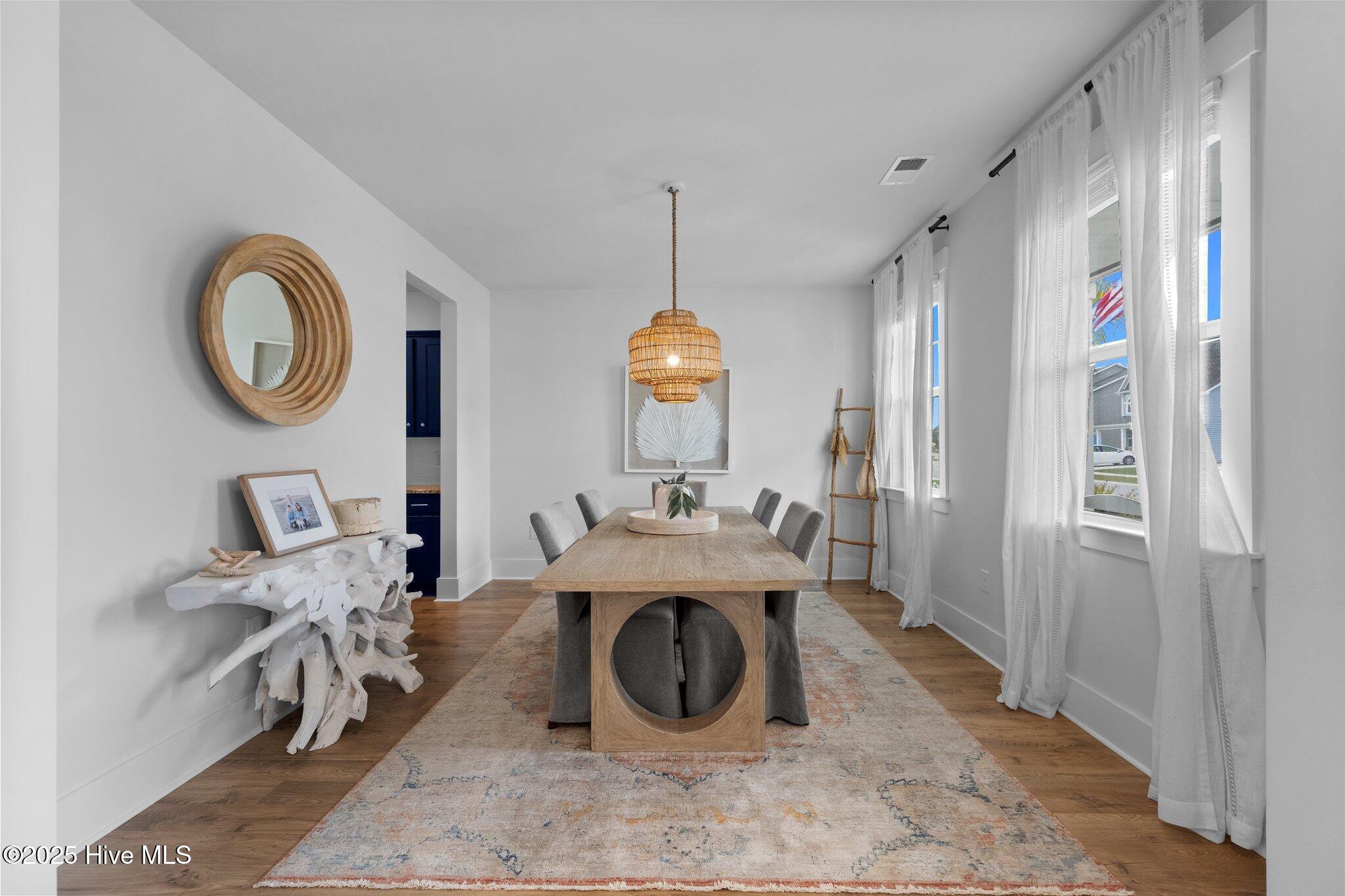 Dining room with a long wooden table, woven pendant light, and tall curtained windows.