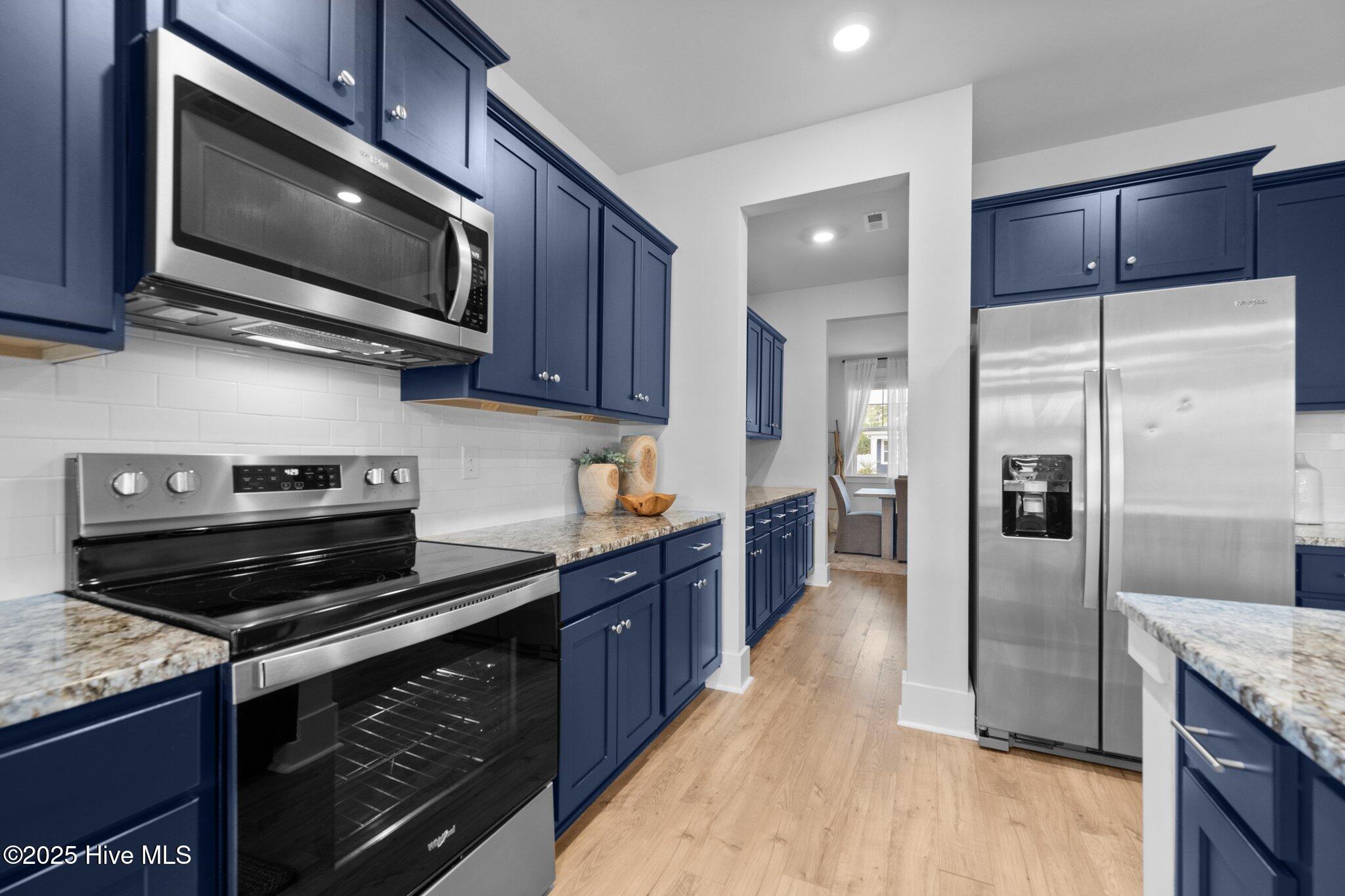 Kitchen with navy cabinets, granite counters, stainless appliances, and a view toward the dining area.