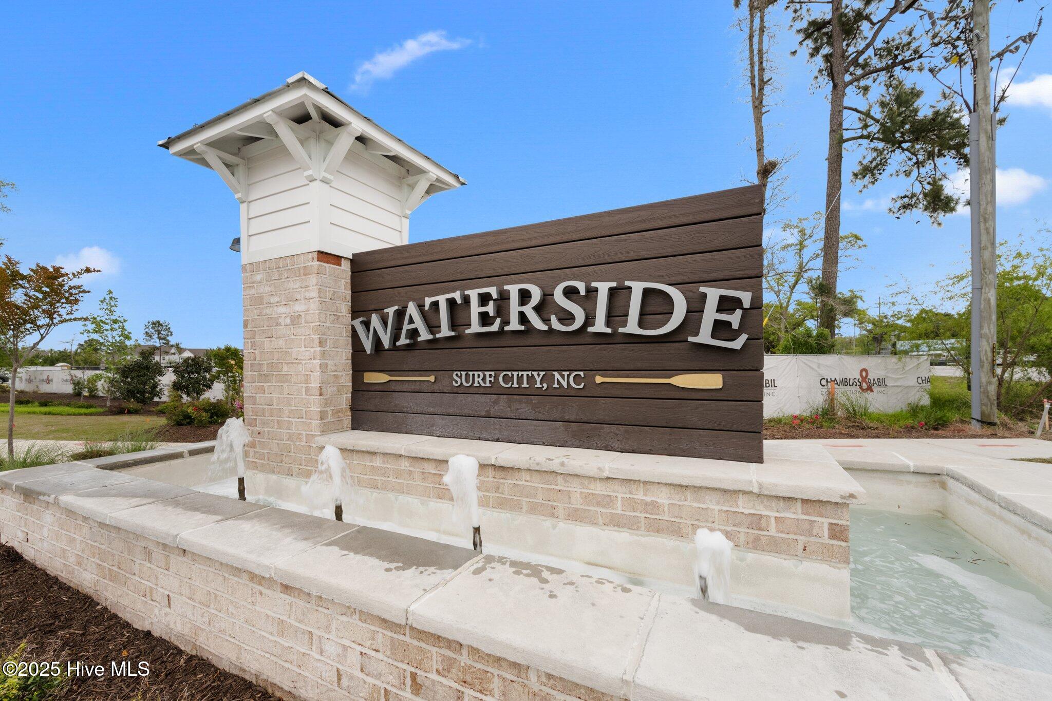 Waterside entrance sign in Surf City, above a brick fountain with several water jets.
