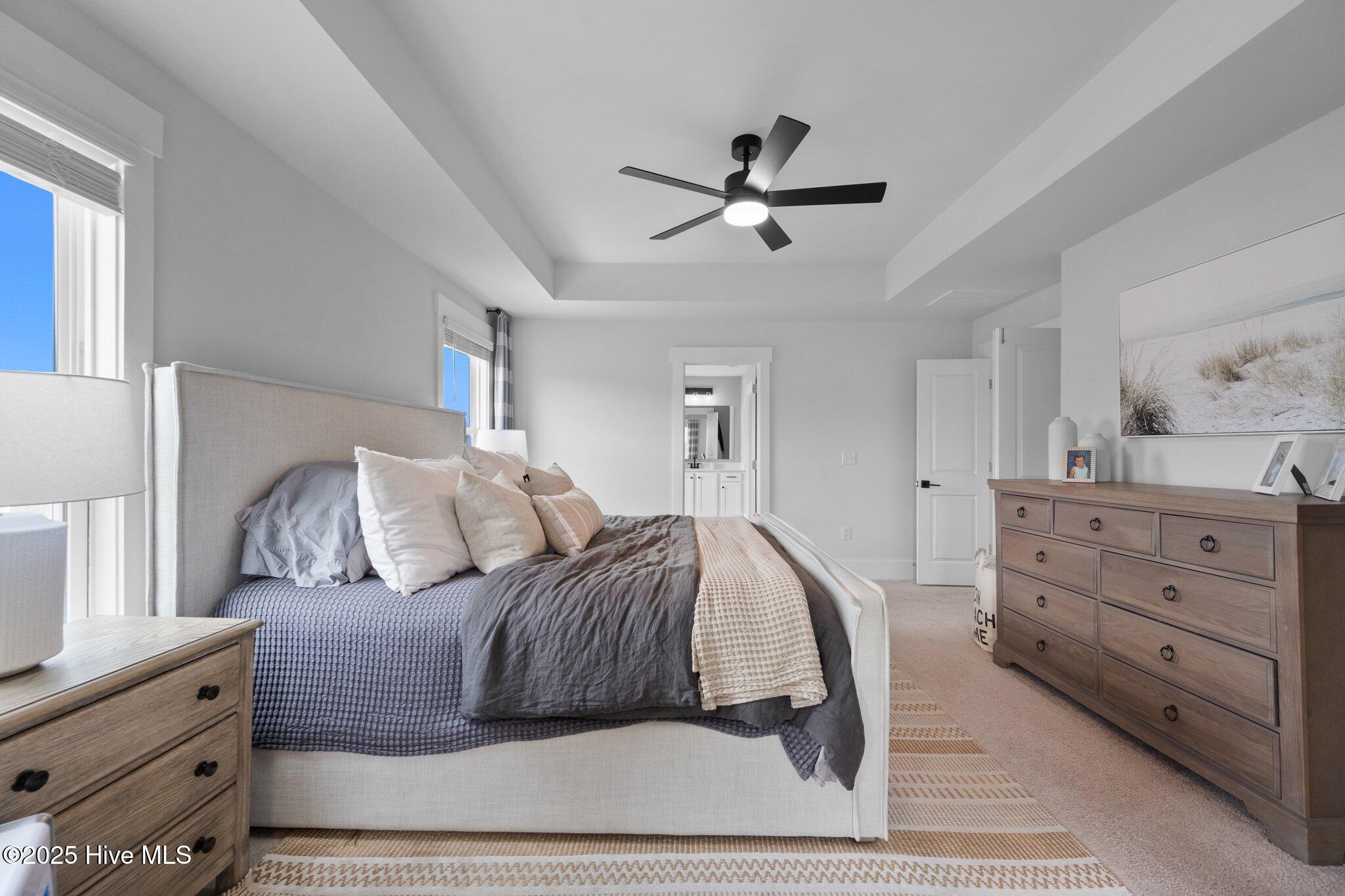 Furnished bedroom with a gray-and-cream bed, wooden dresser, and ceiling fan.