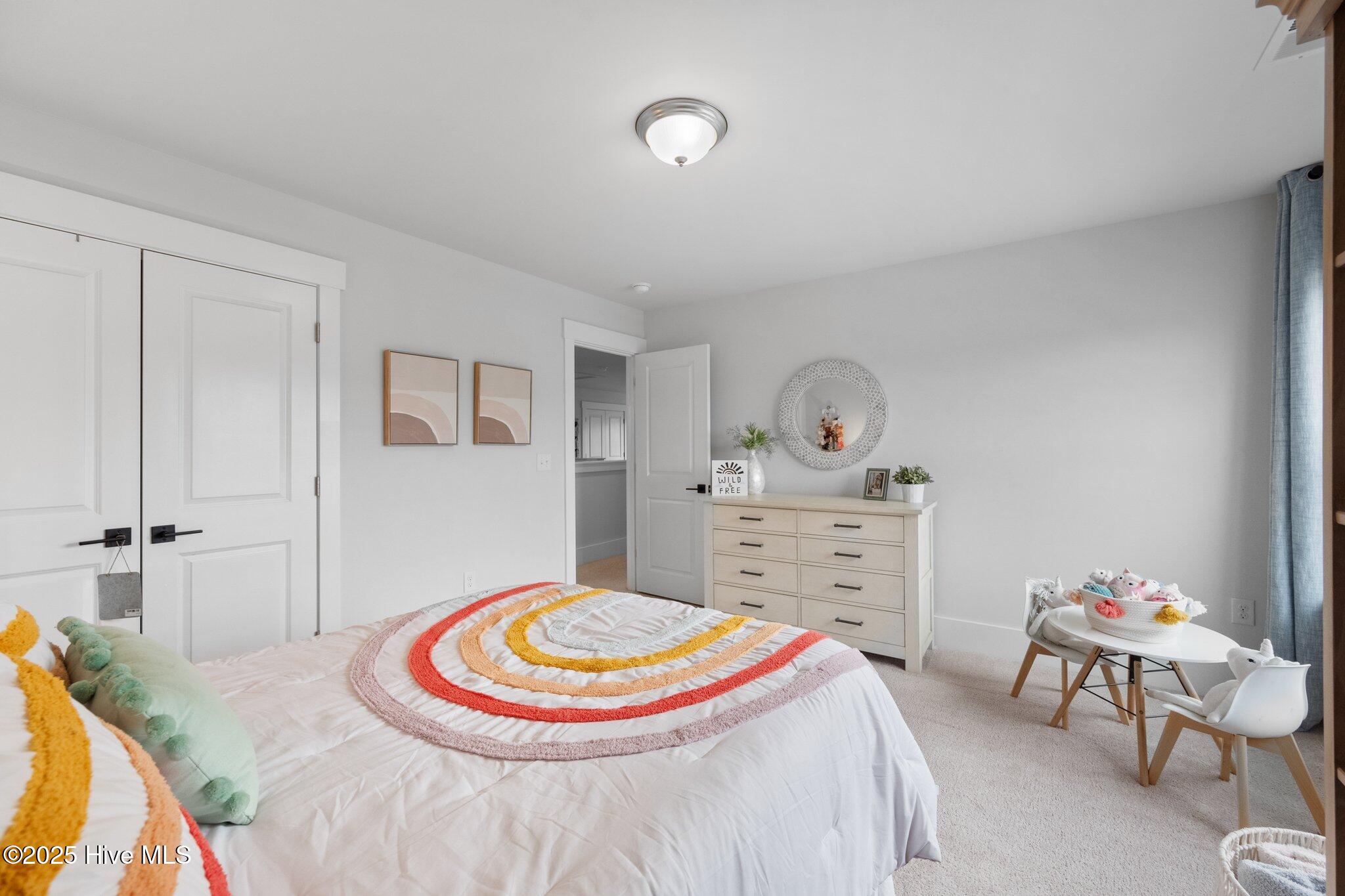 Bedroom with colorful rainbow-striped bedding, a white dresser, and a small table and chairs.