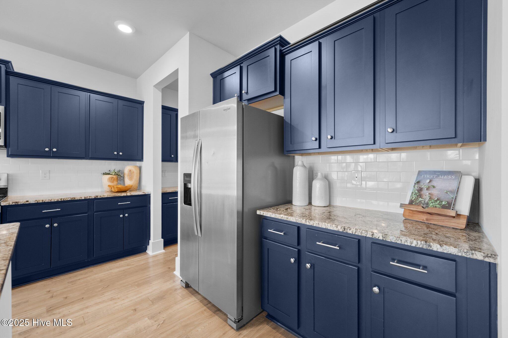 Kitchen with navy cabinets, granite countertops, and a stainless-steel refrigerator.