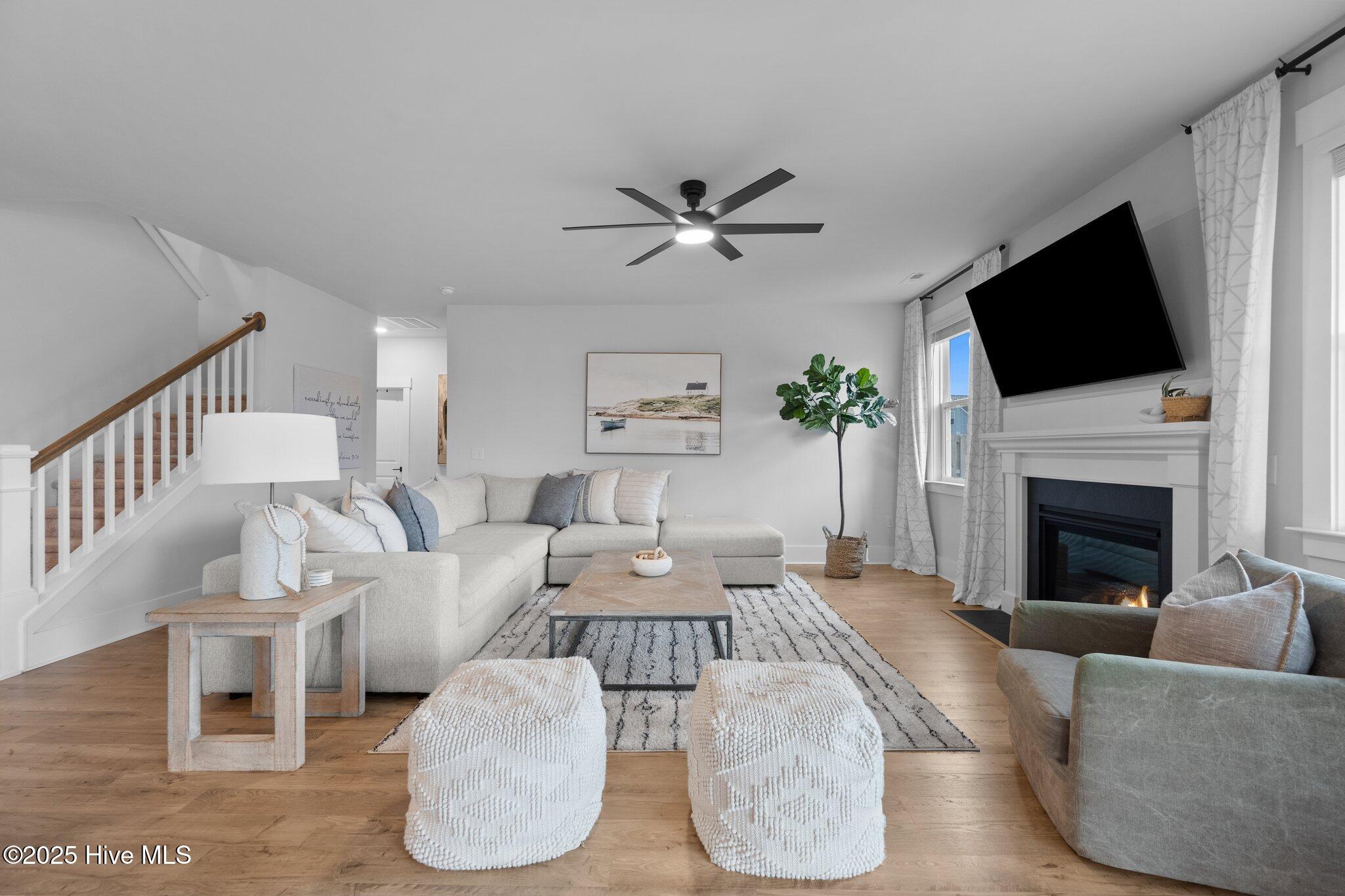 Staged living room with a sectional sofa, staircase, and fireplace beneath a wall-mounted television.
