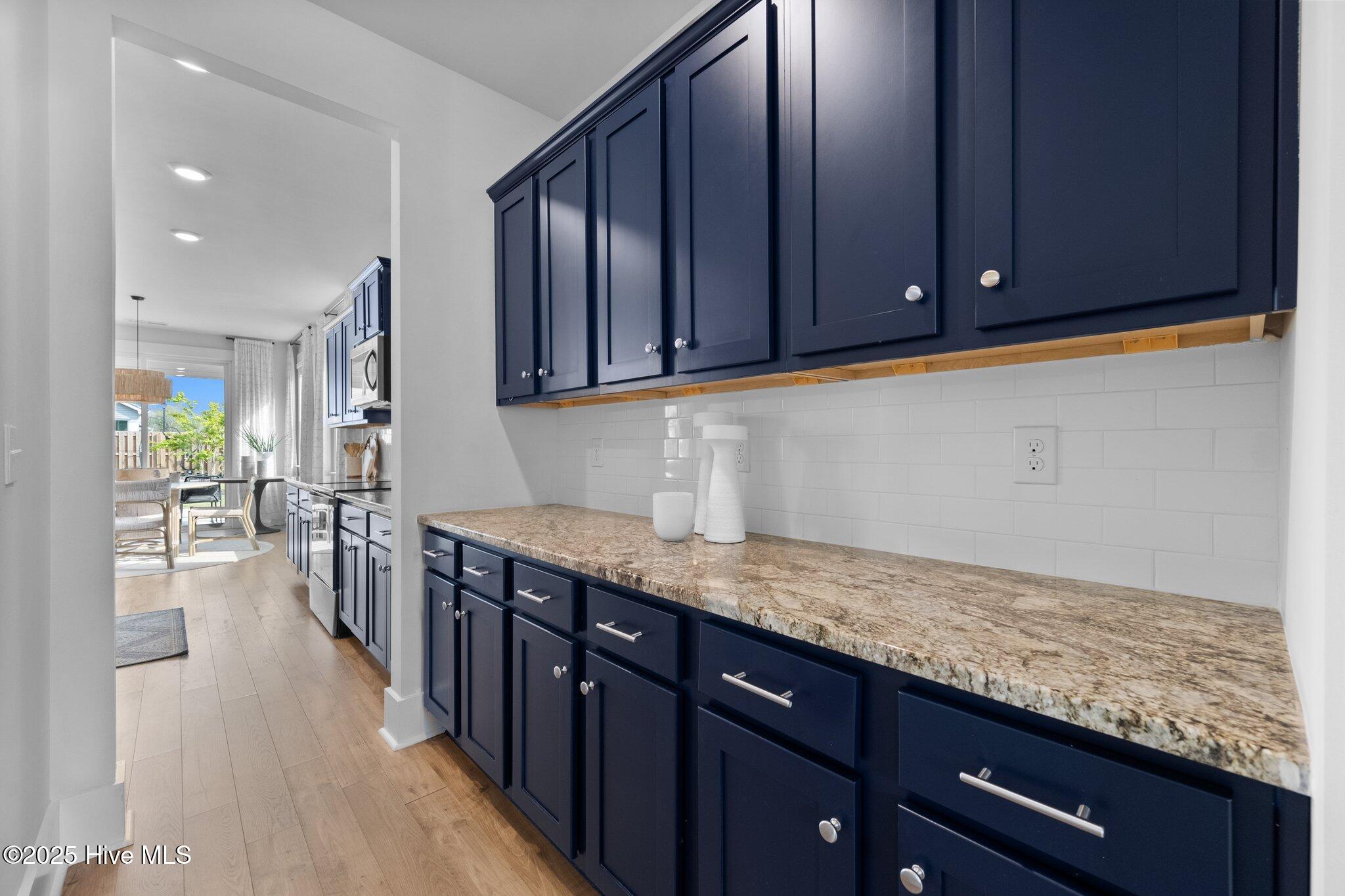 Kitchen with navy cabinets, granite countertops, and white subway tile, opening to a bright dining area.