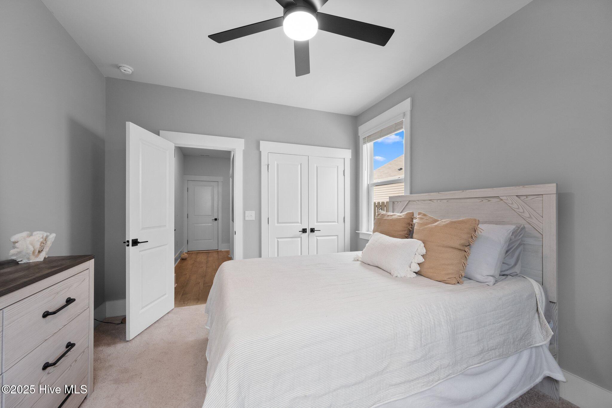 Furnished bedroom with a white bed, tan accent pillows, light wood furniture, and a ceiling fan.