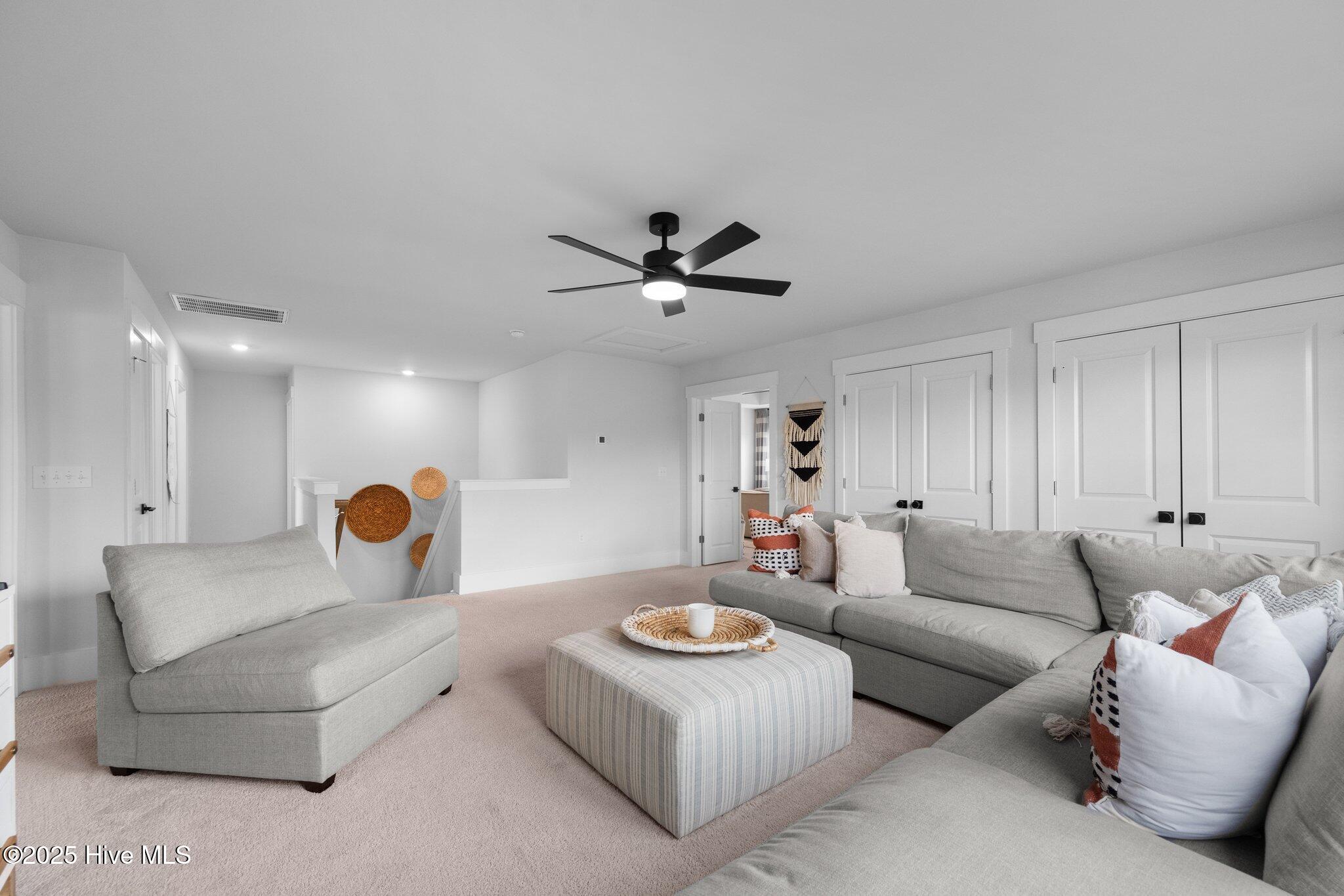 Living room with gray sofas, a striped ottoman, and a black ceiling fan.