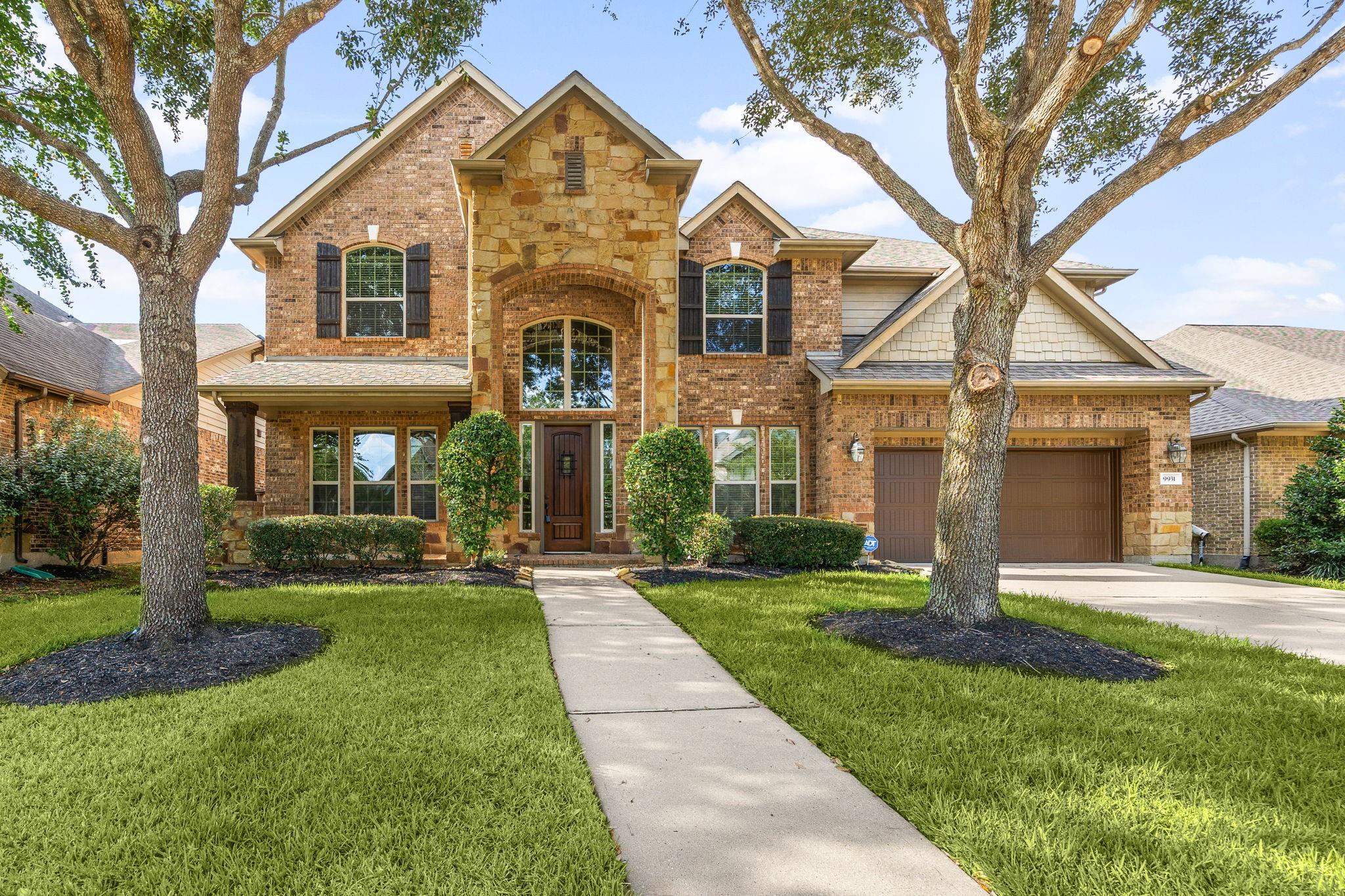 Two-story brick and stone house with a central arched entry, double garage, and mature trees.