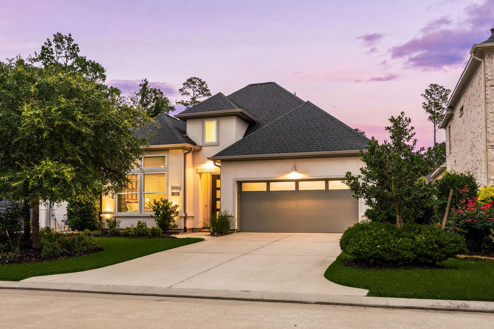 Modern two-story home with a dark hipped roof, landscaped yard, and lit garage at dusk.