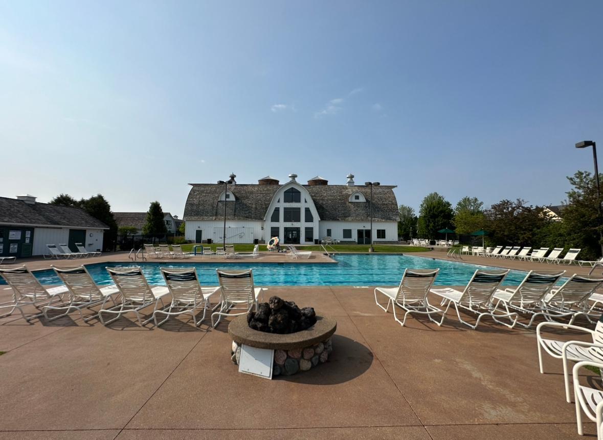 Community swimming pool with lounge chairs, stone fire pit, and barn-style clubhouse.
