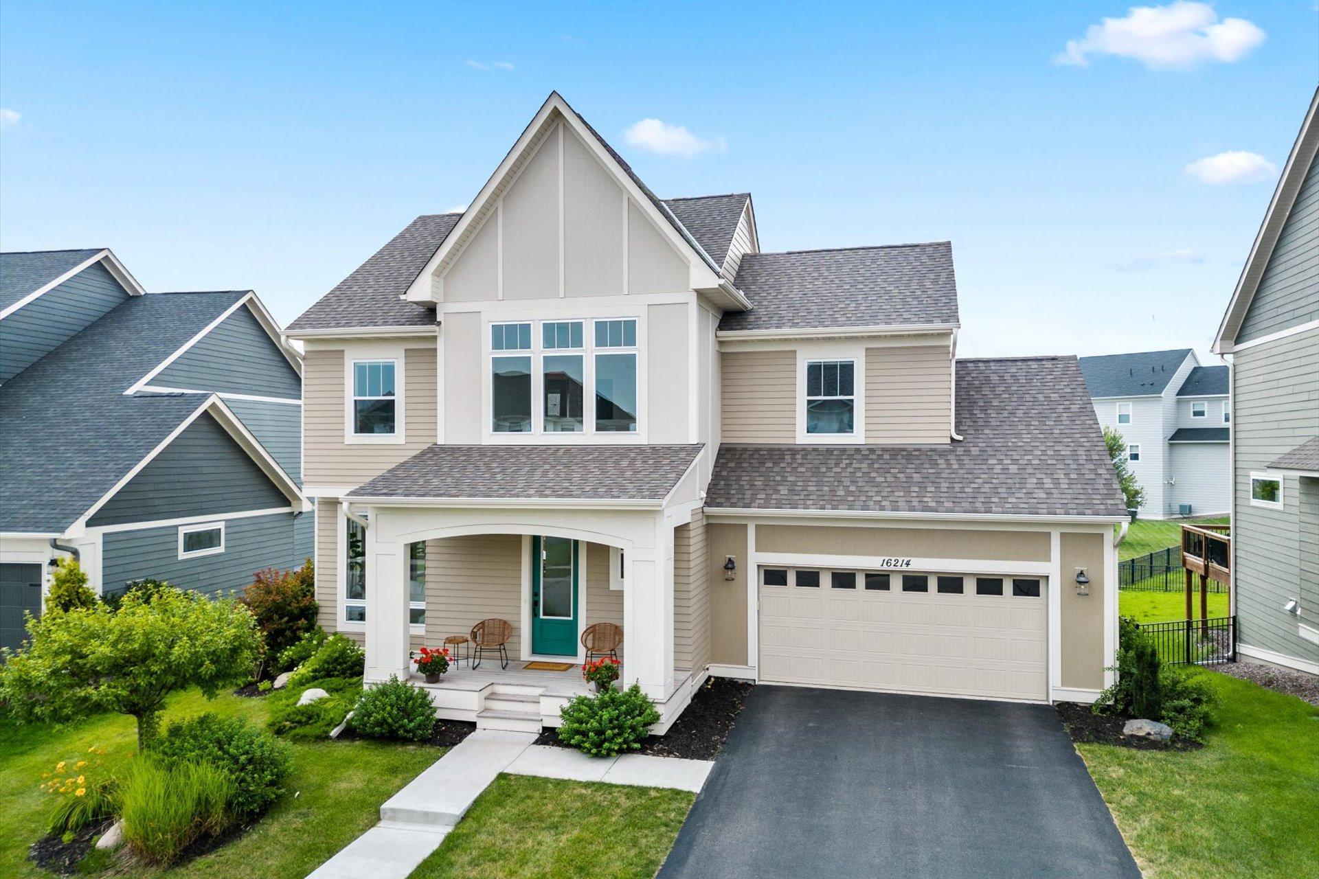 Two-story beige house with a teal front door, covered porch, and attached garage.