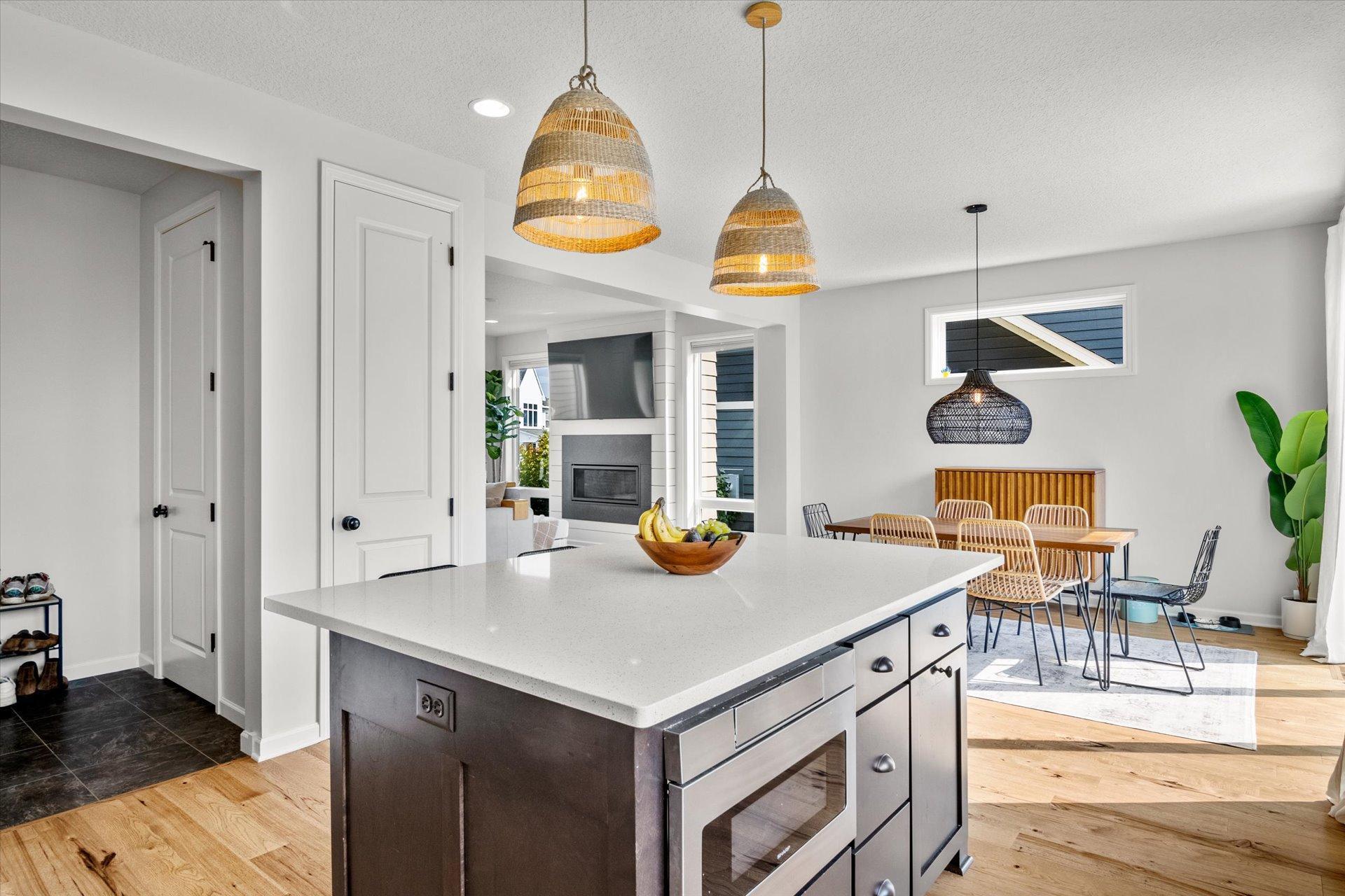 Open kitchen and dining area with a quartz island, woven pendant lights, and an adjoining fireplace.