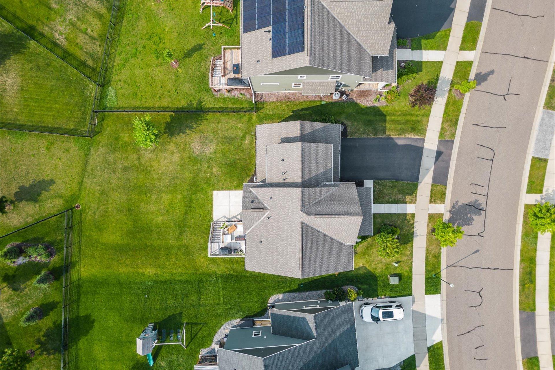 Aerial view of a home with rooftop solar panels, decks, and a fenced backyard.