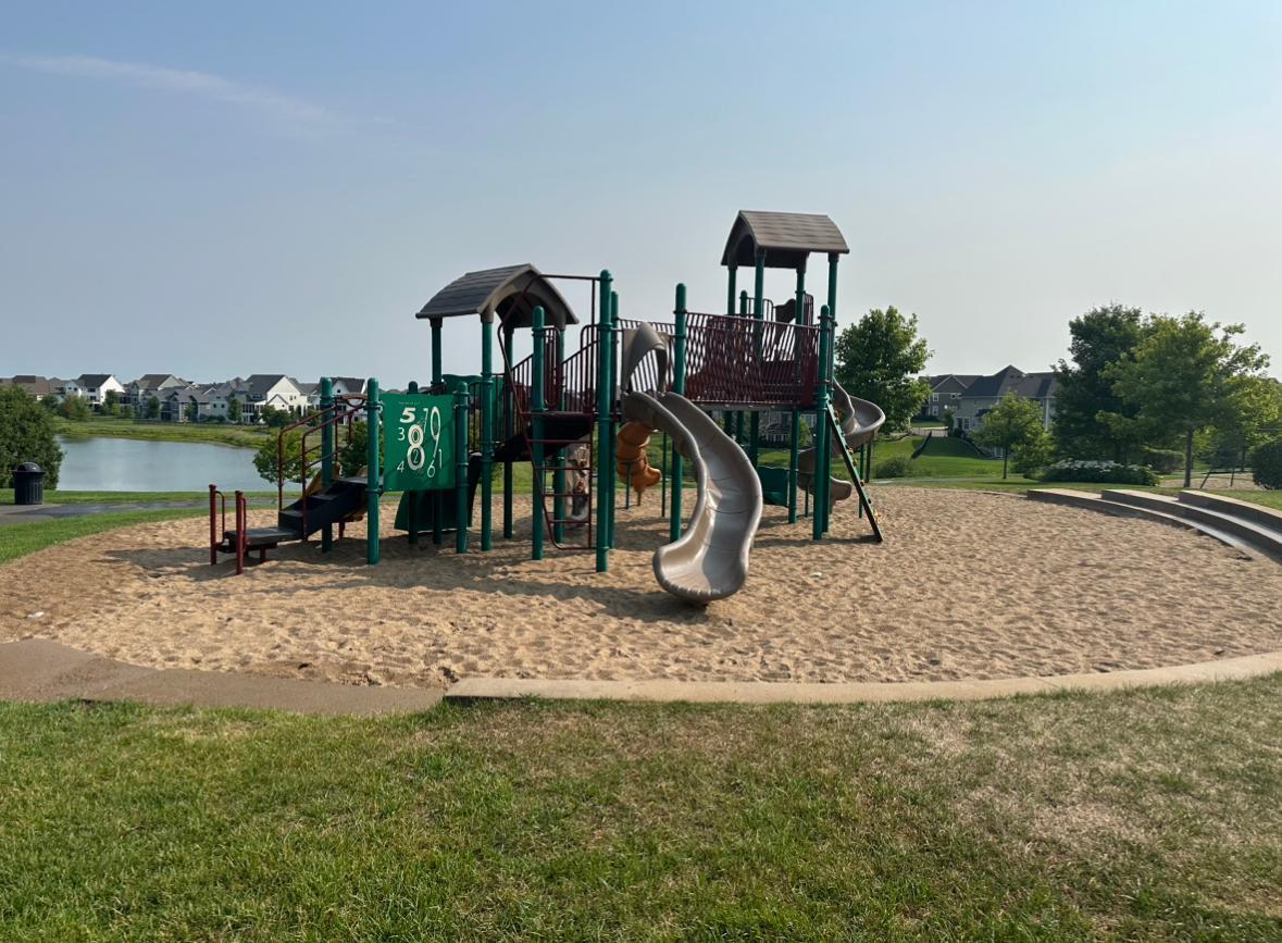 Neighborhood playground with a large play structure and slides beside a pond.