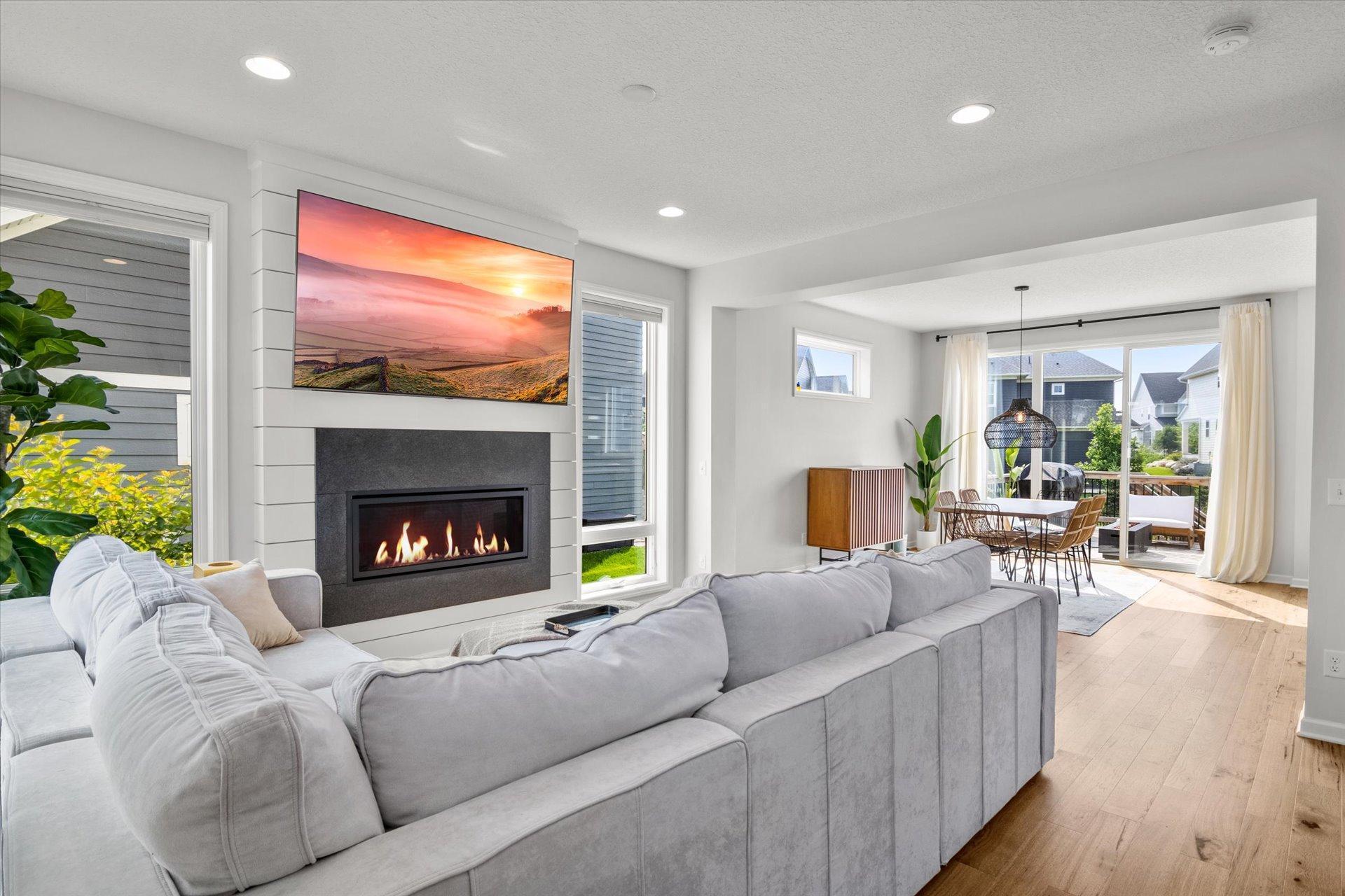 Living room with a gray sectional, modern fireplace, and dining area opening to a deck.
