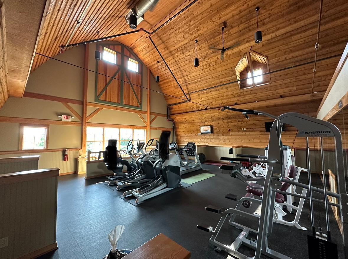 Fitness room with cardio and weight-training equipment beneath a vaulted wood ceiling.