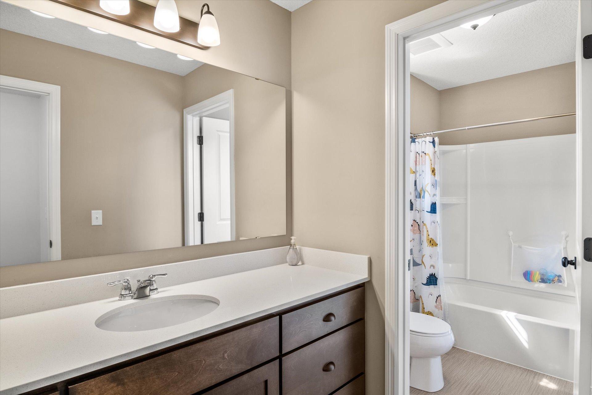 Bathroom with a long vanity and mirror beside a bathtub with an animal-print shower curtain.