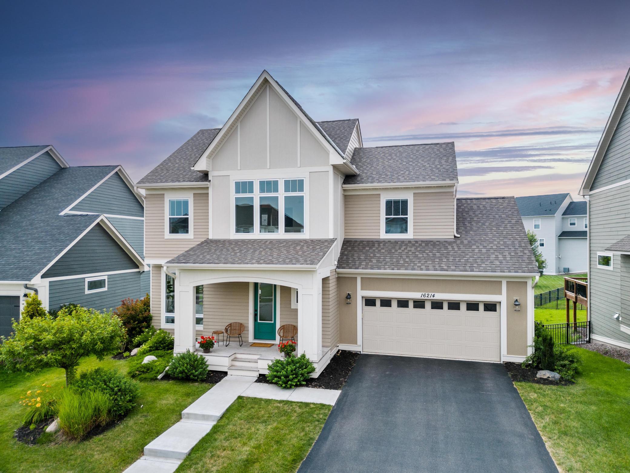 Two-story beige home with a covered porch, white trim, and attached garage at dusk.