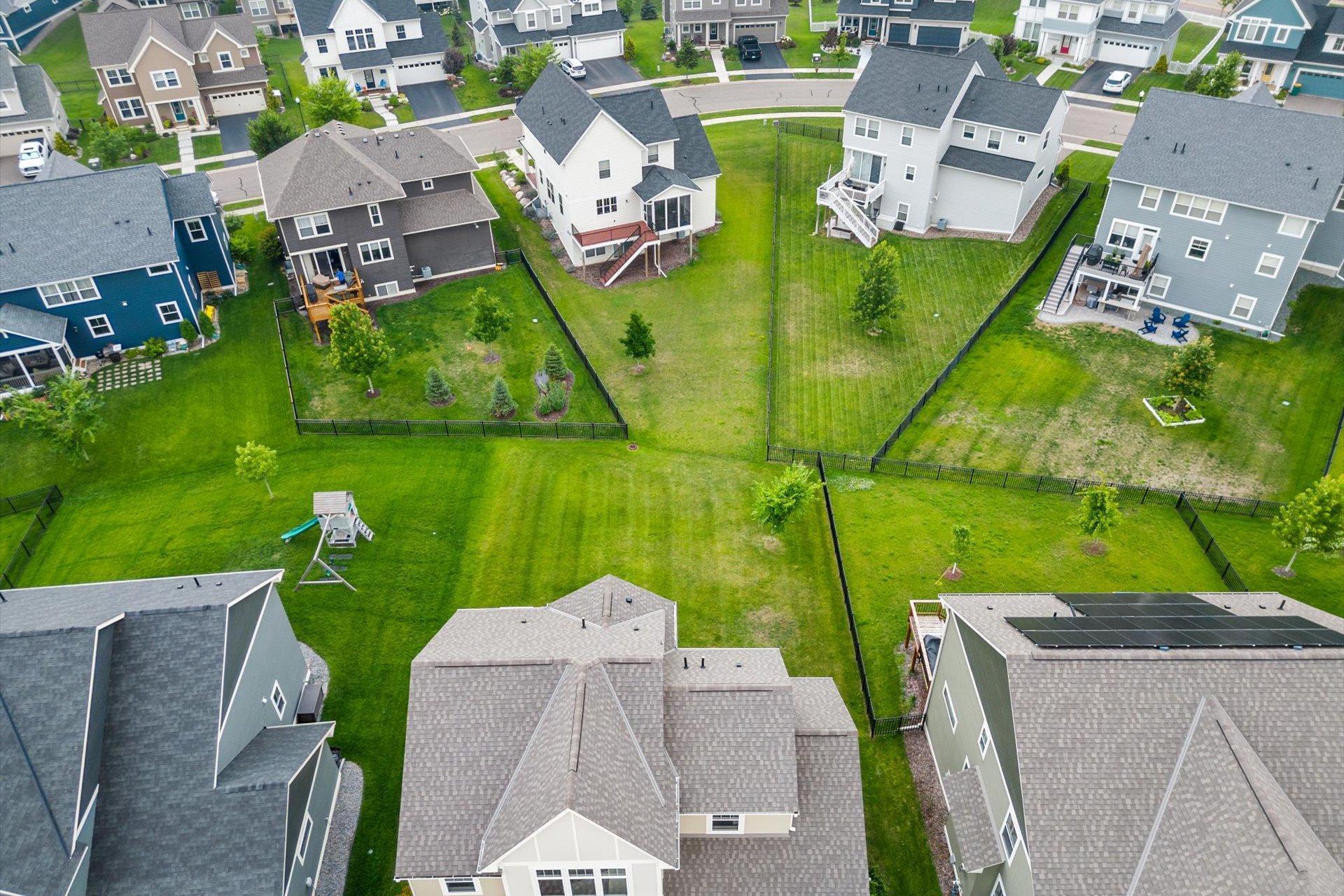 Aerial view of fenced backyards and homes surrounding a broad green lawn.