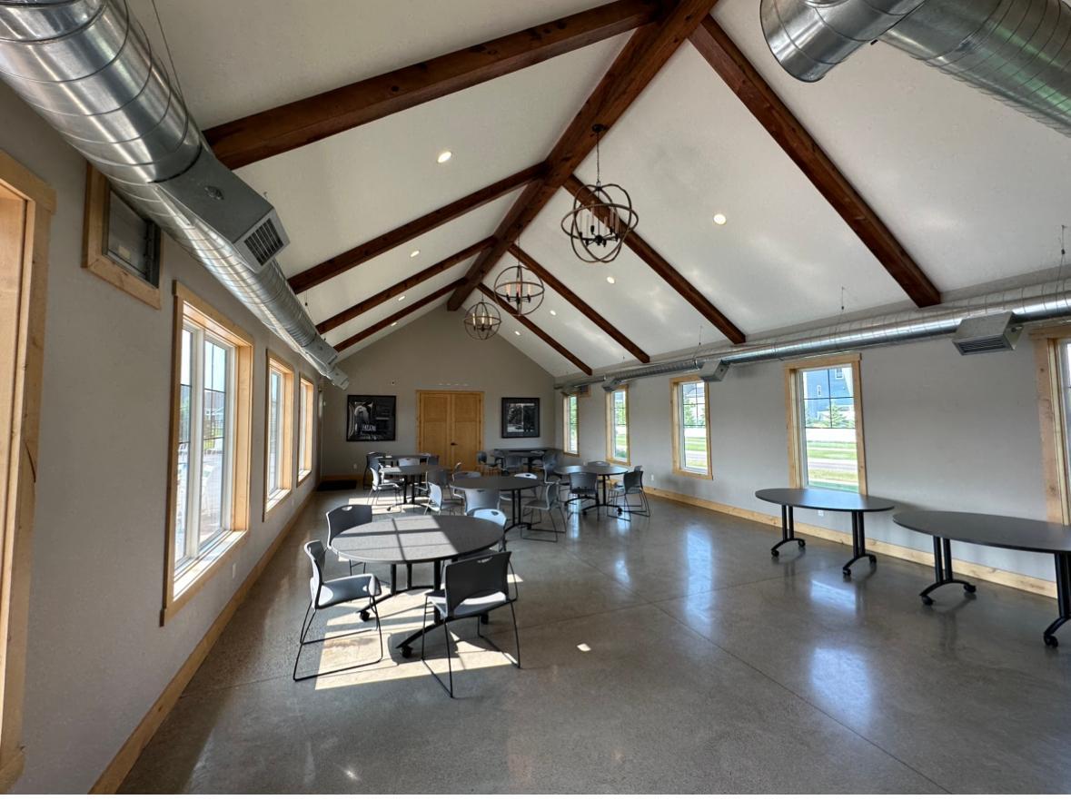 Communal room with vaulted timber beams, exposed ductwork, and tables by tall windows.