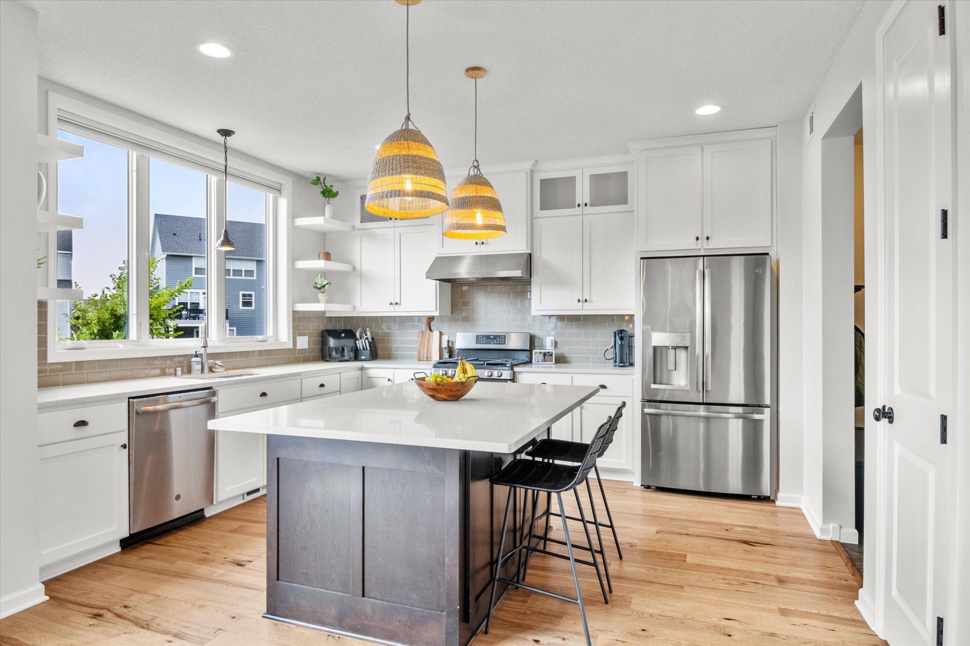 Bright white kitchen with a gray island, stainless steel appliances, and woven pendant lights.