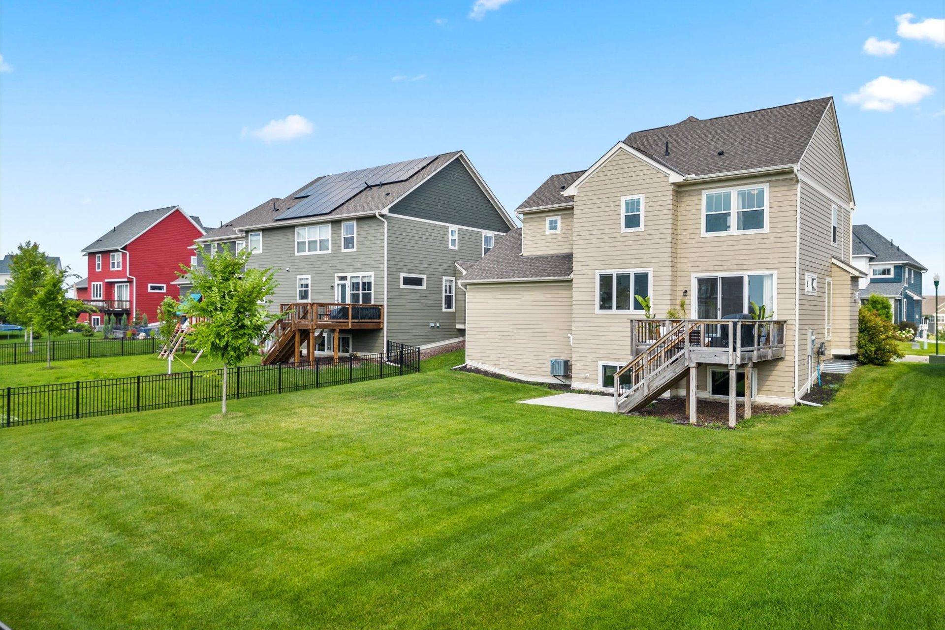 Beige two-story home with a raised wooden deck overlooking a broad fenced lawn.