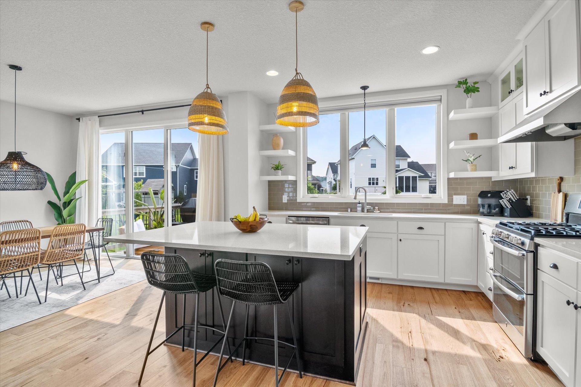 Bright kitchen with a dark island, white cabinets, woven pendant lights, and windows overlooking neighboring homes.