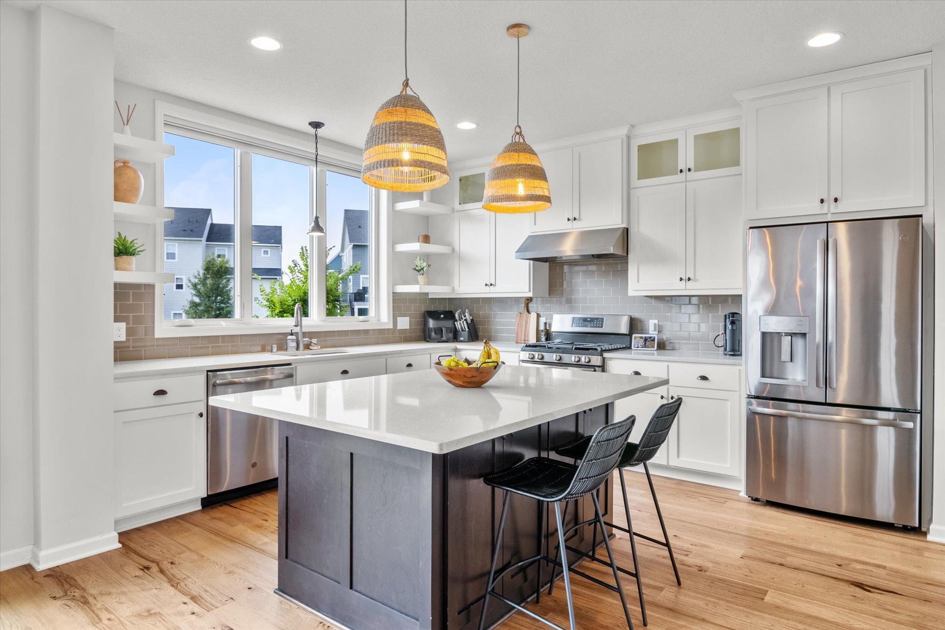 Bright kitchen with a large dark island, white cabinetry, stainless steel appliances, and woven pendant lights.